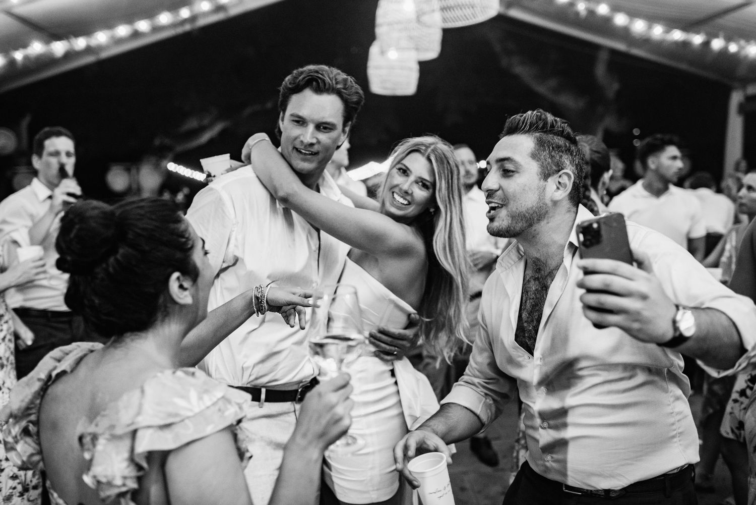 Black and white photo series showing couples dancing and embracing at a wedding reception with string lights overhead.