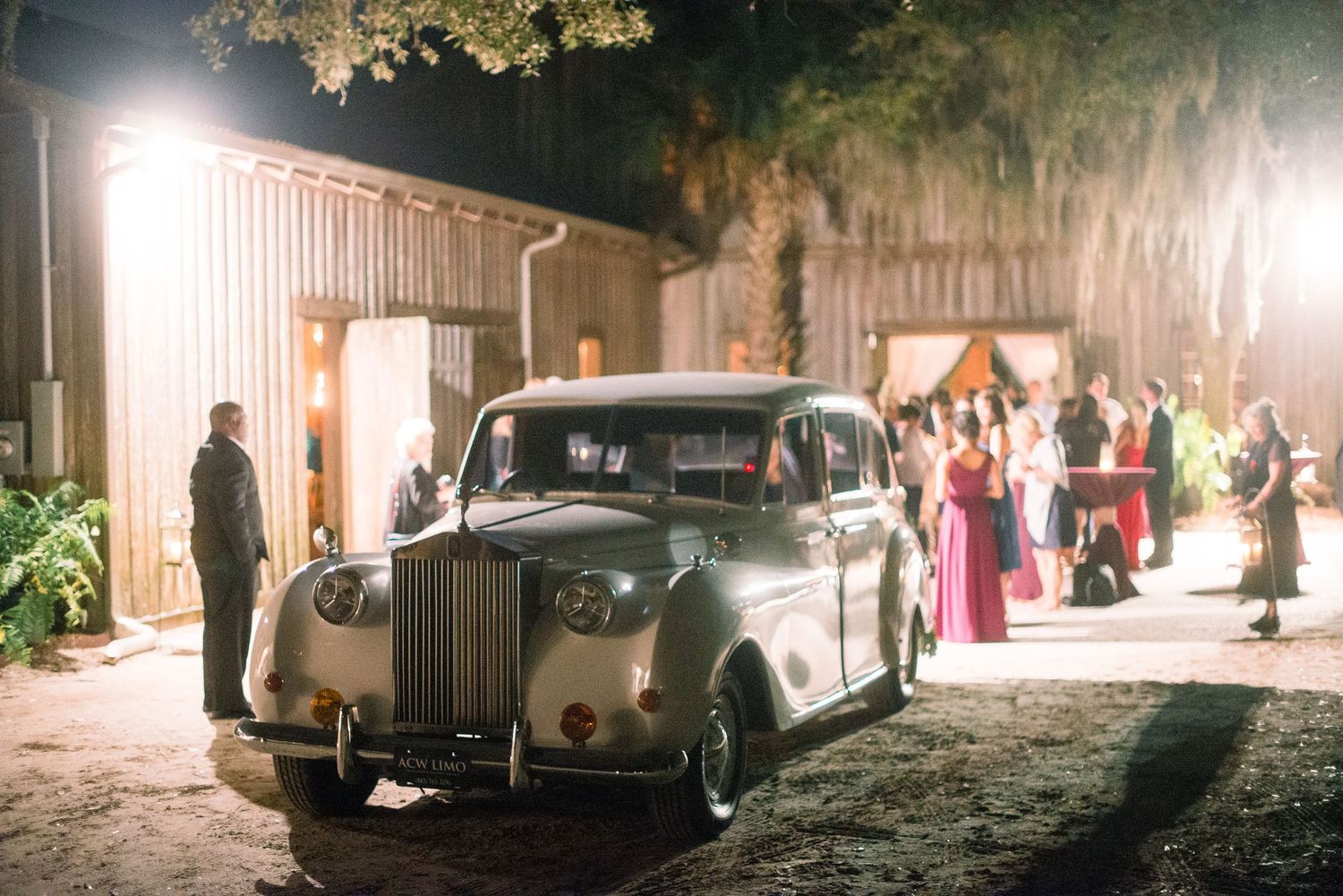 Classic vintage cars line up outside an elegant venue at night with warm lighting creating a romantic atmosphere.