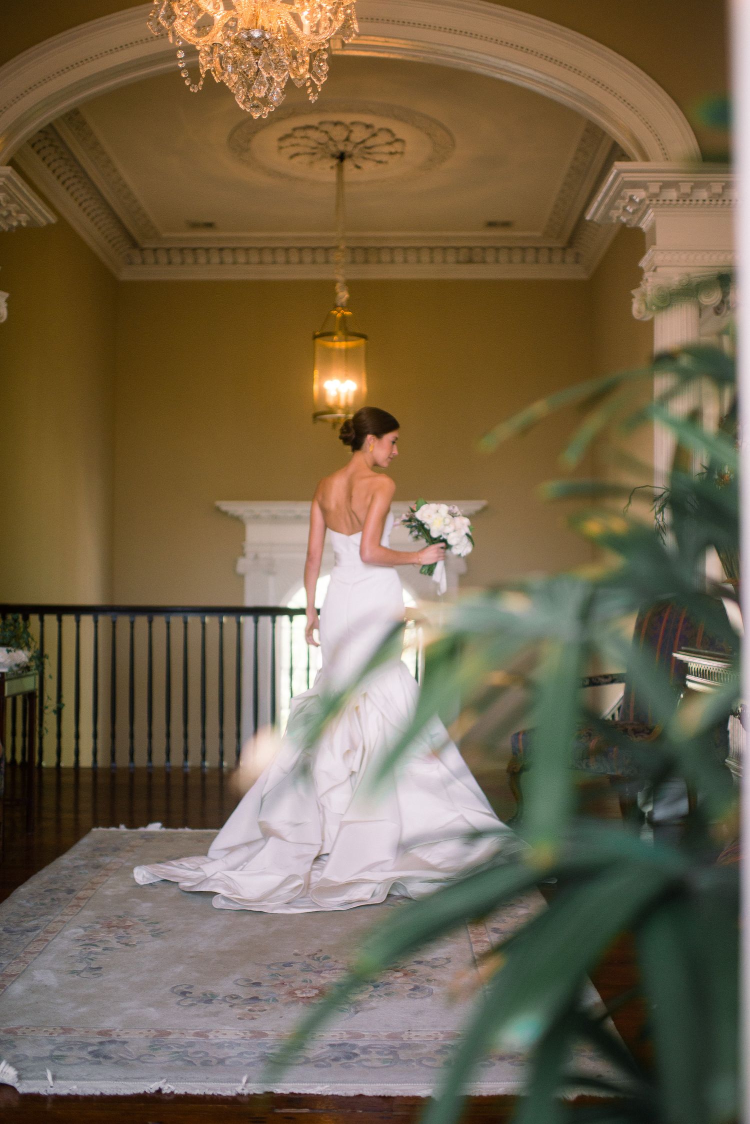 Elegant bride in white gown poses in a grand ballroom with crystal chandeliers and ornate architectural details.