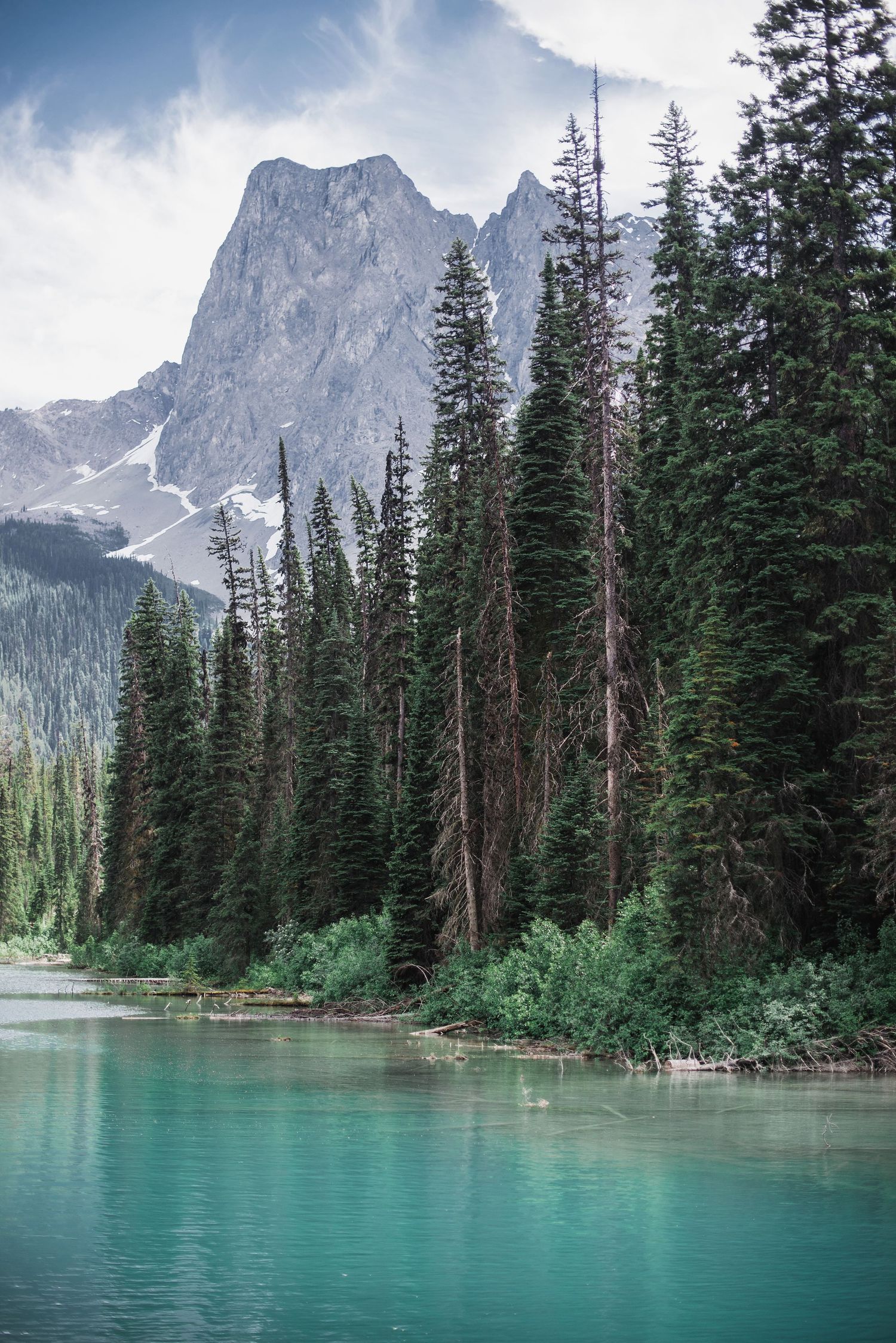 Emerald lake reflects towering mountain peaks through a forest of evergreen trees in the Canadian wilderness.