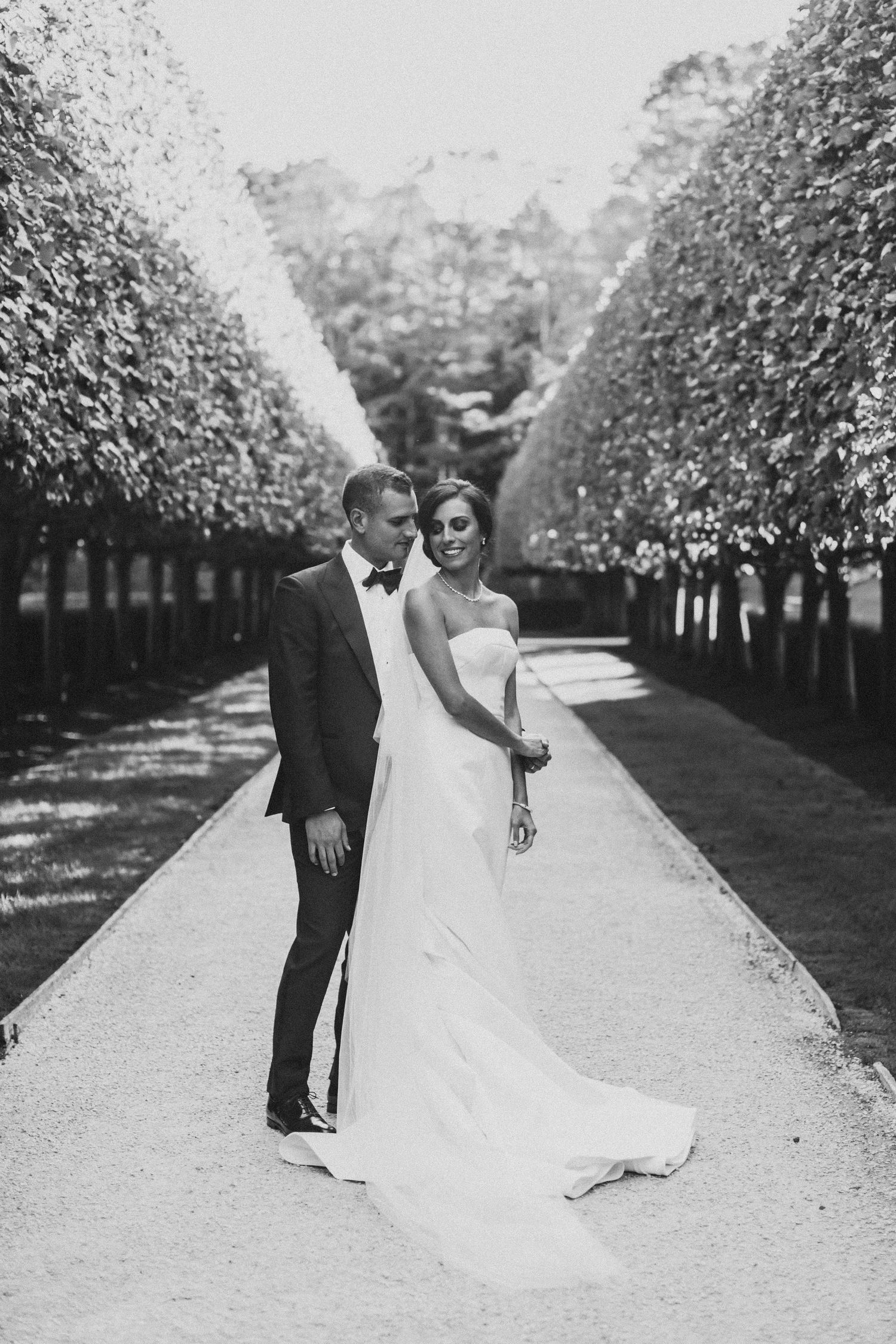 Black and white wedding portraits of couple dancing along a tree-lined path.