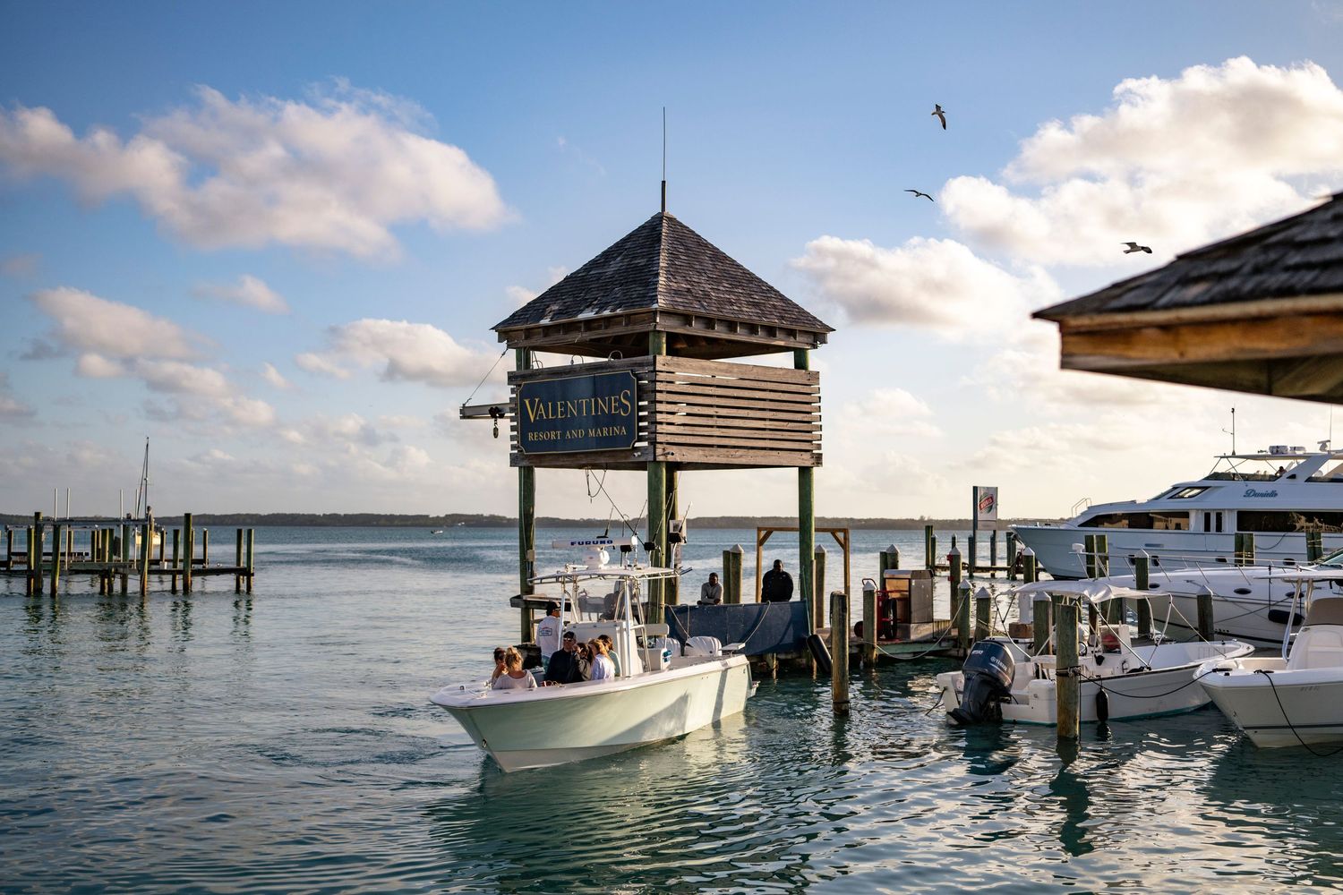 Boats and gazebos dot the crystal clear waters of a tropical resort pier at sunset.