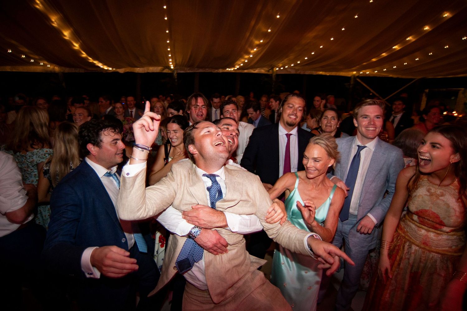 Wedding reception party scene with string lights and dancing guests in dimly lit venue.