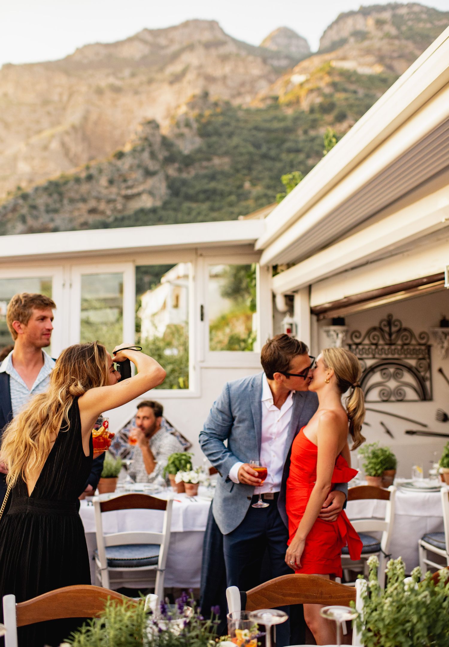 People enjoying drinks and conversation on an outdoor patio with mountain views during a social gathering.