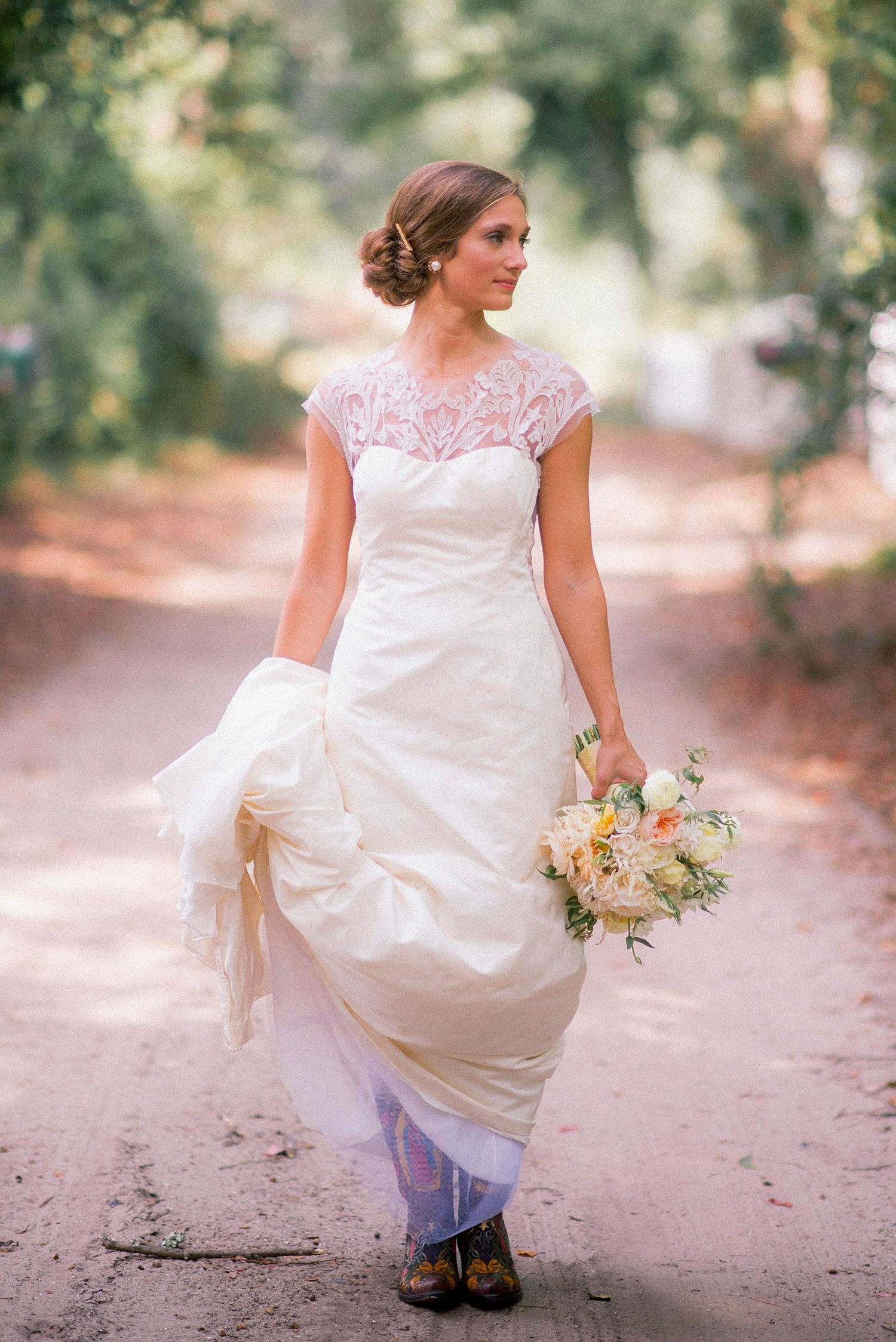 Bride in a flowing white lace gown twirls playfully on a rustic dirt path.
