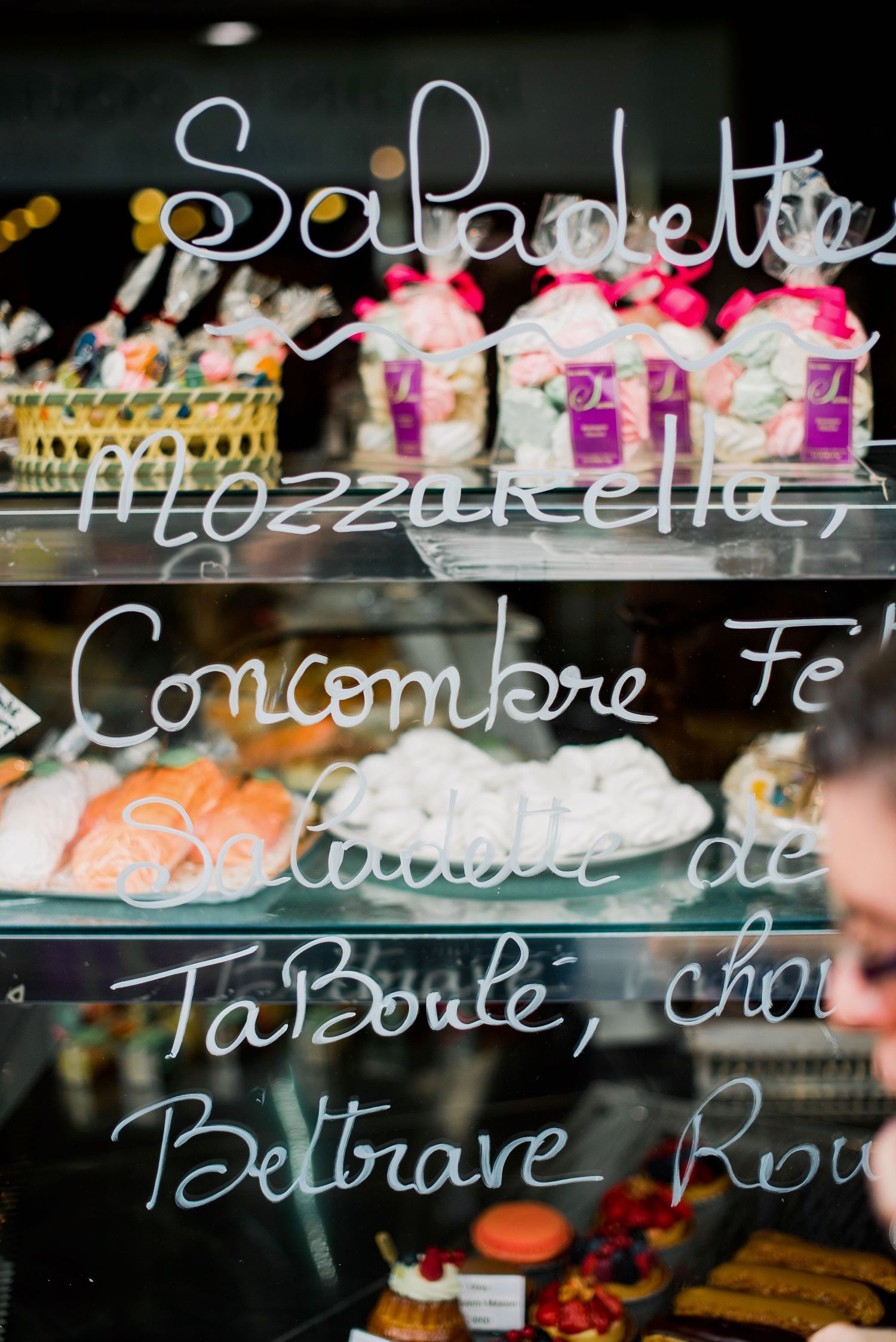 Handwritten menu text on glass display case in a French patisserie shop.