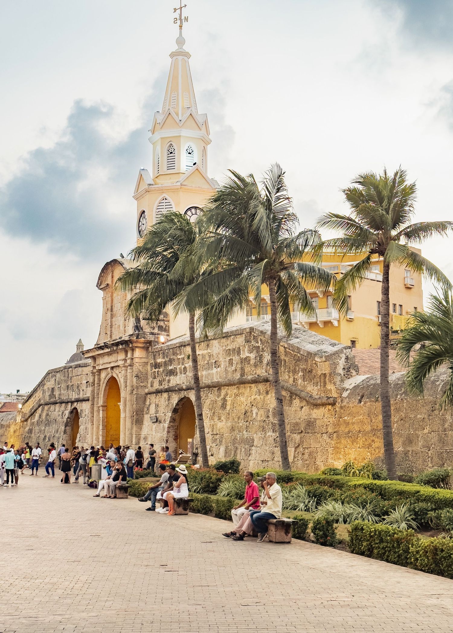 Historic stone church in Cartagena with palm trees and Spanish colonial architecture under cloudy skies.
