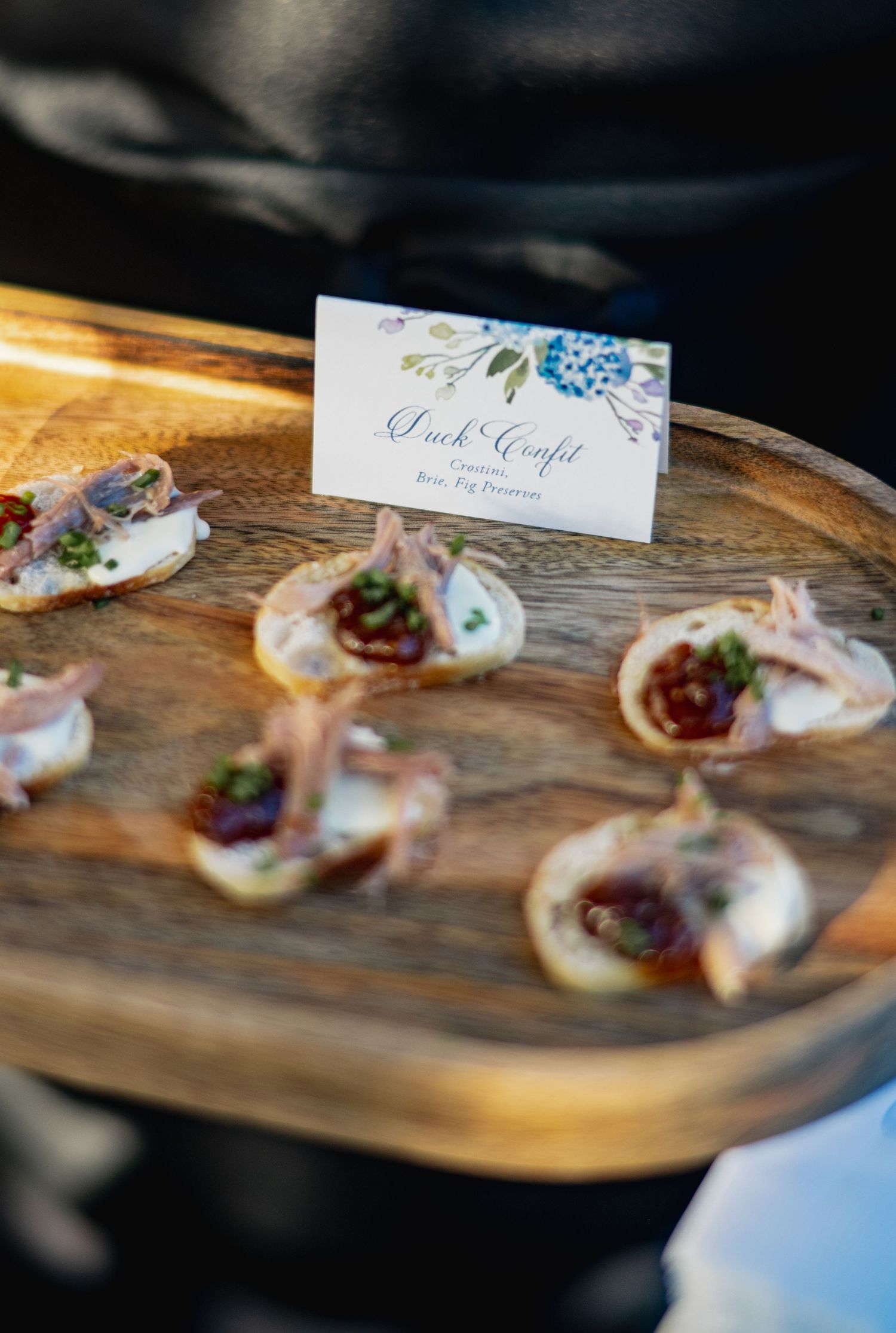 Elegant appetizers served on a rustic wooden platter with name cards at what appears to be a catered event.