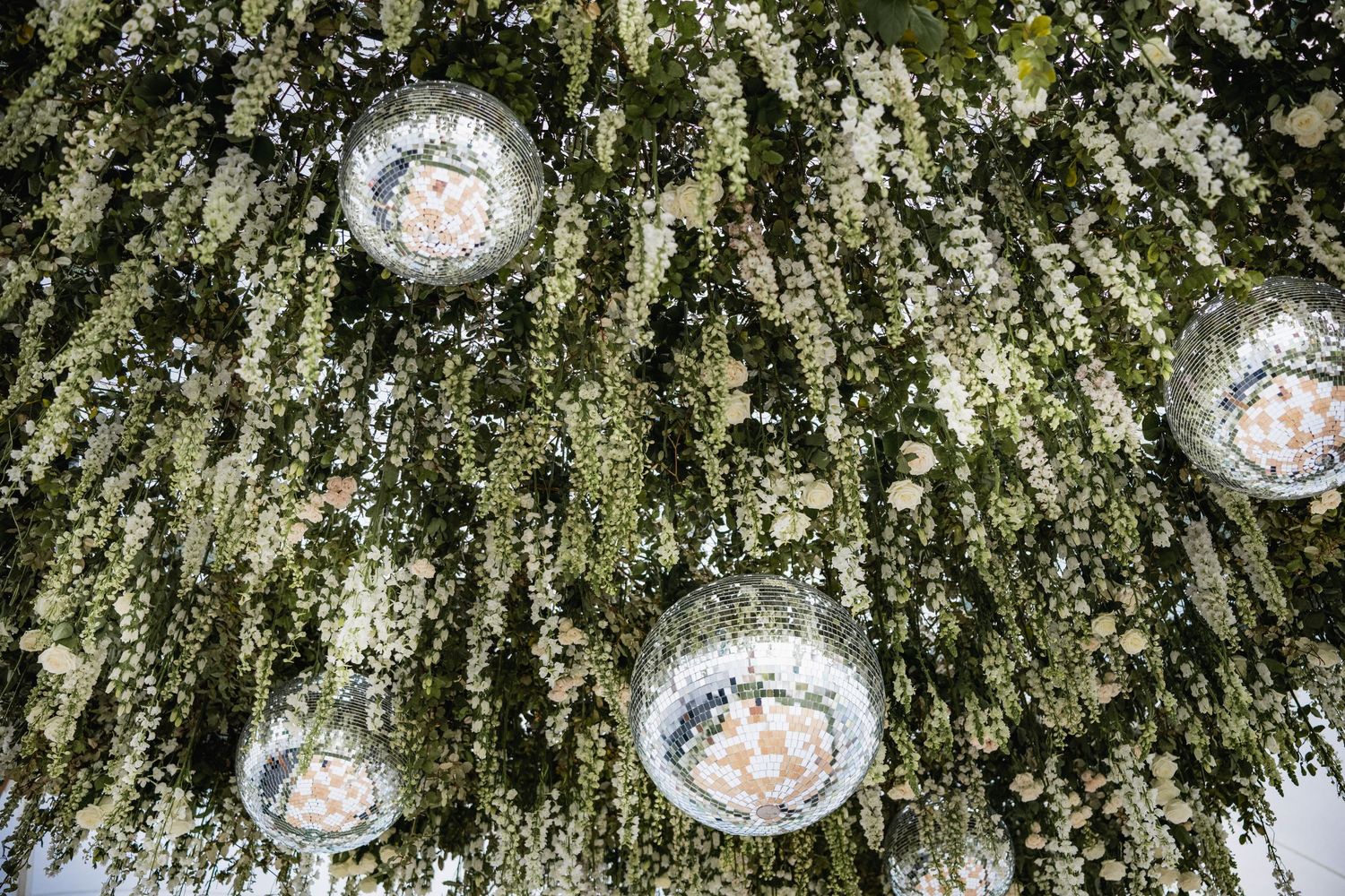 Crystal chandeliers hanging among cascading white floral installations and greenery for an elegant wedding reception.