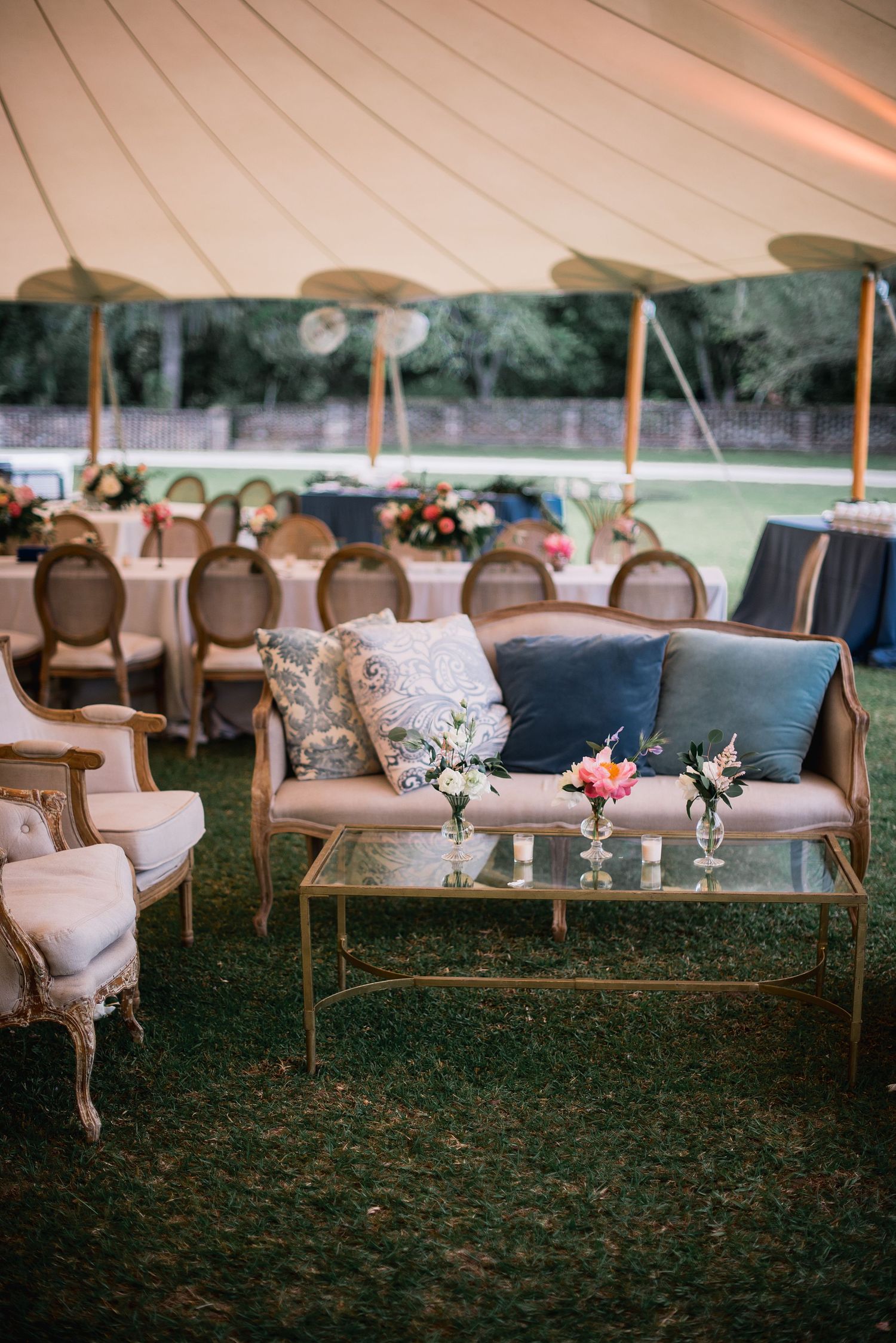 Elegant vintage-style lounge seating arranged outdoors under a tent with floral arrangements and soft lighting.