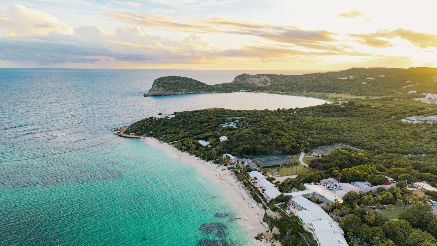 Sunset aerial view of a tropical beach resort with white sand and emerald waters.