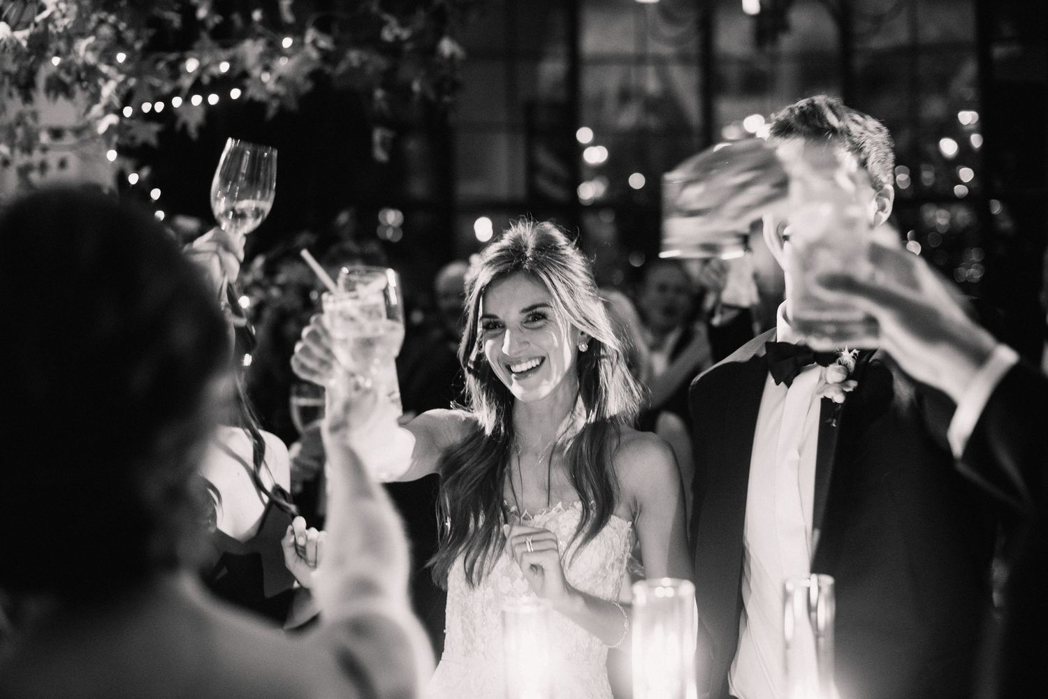 Wedding reception guests raise their glasses in celebration during an elegant candlelit dinner party.