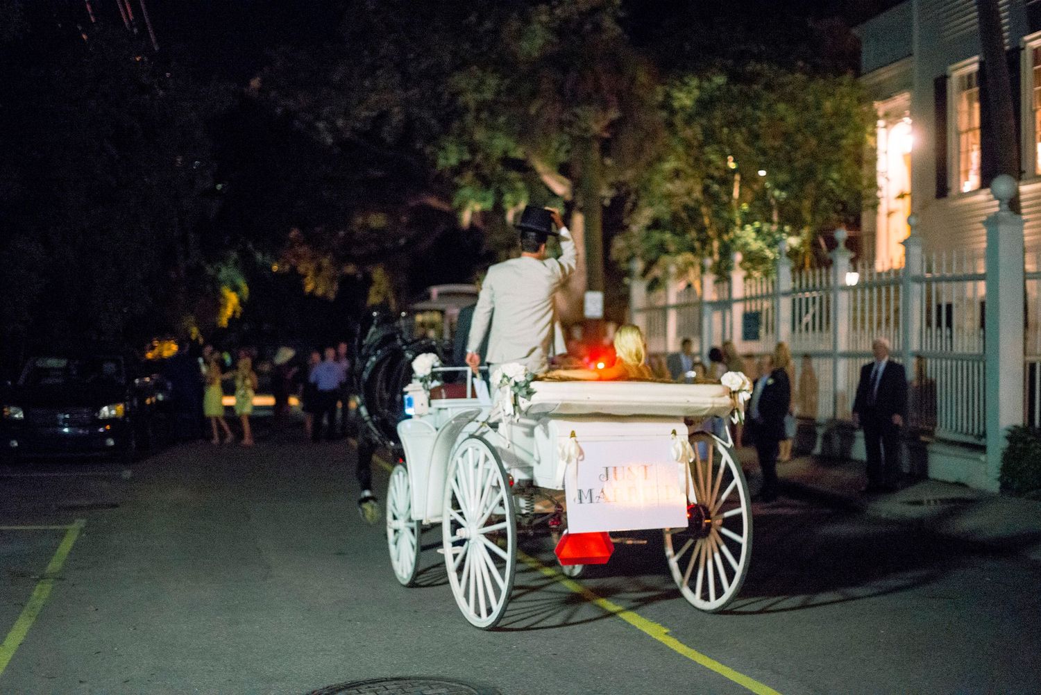 A white horse-drawn carriage illuminated at night on a dark street with buildings in the background.