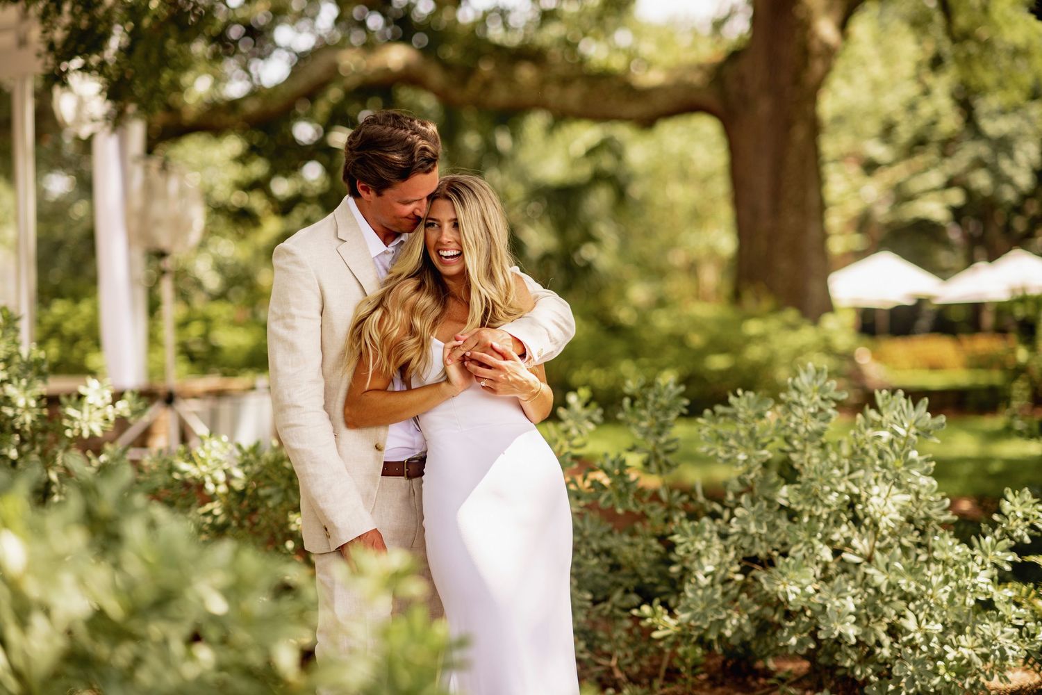 A couple in wedding attire shares a romantic moment in a lush garden setting during their outdoor ceremony.