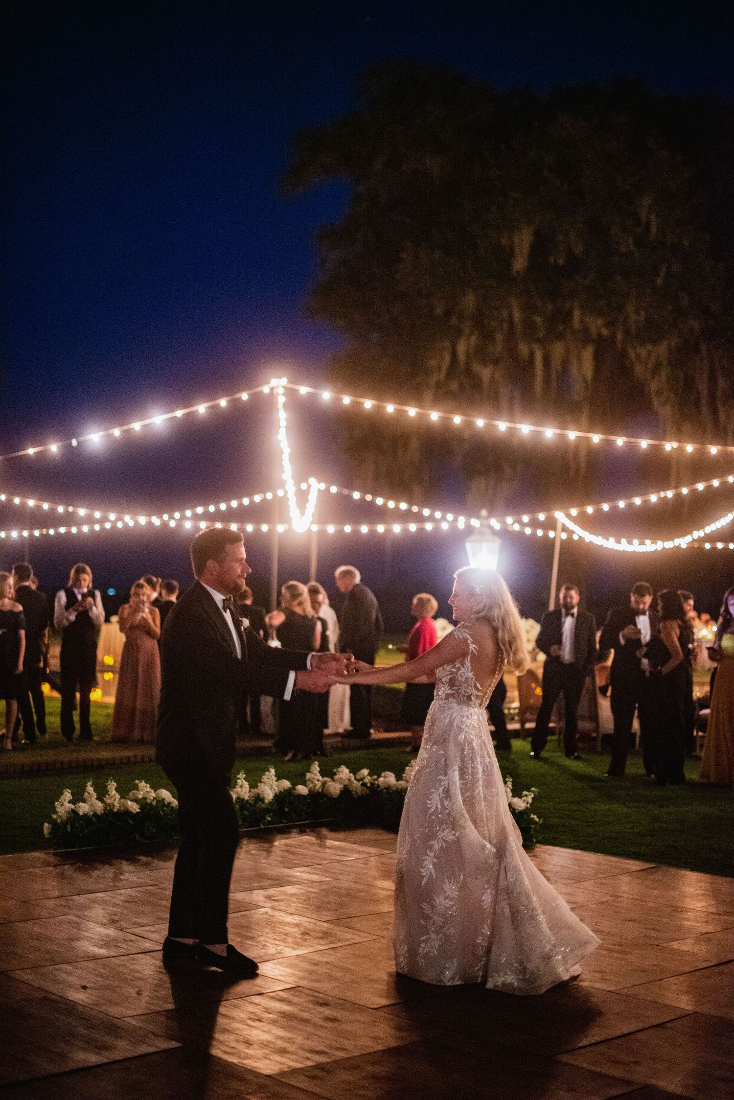 A romantic evening wedding reception dance under glowing string lights on an outdoor stone patio.