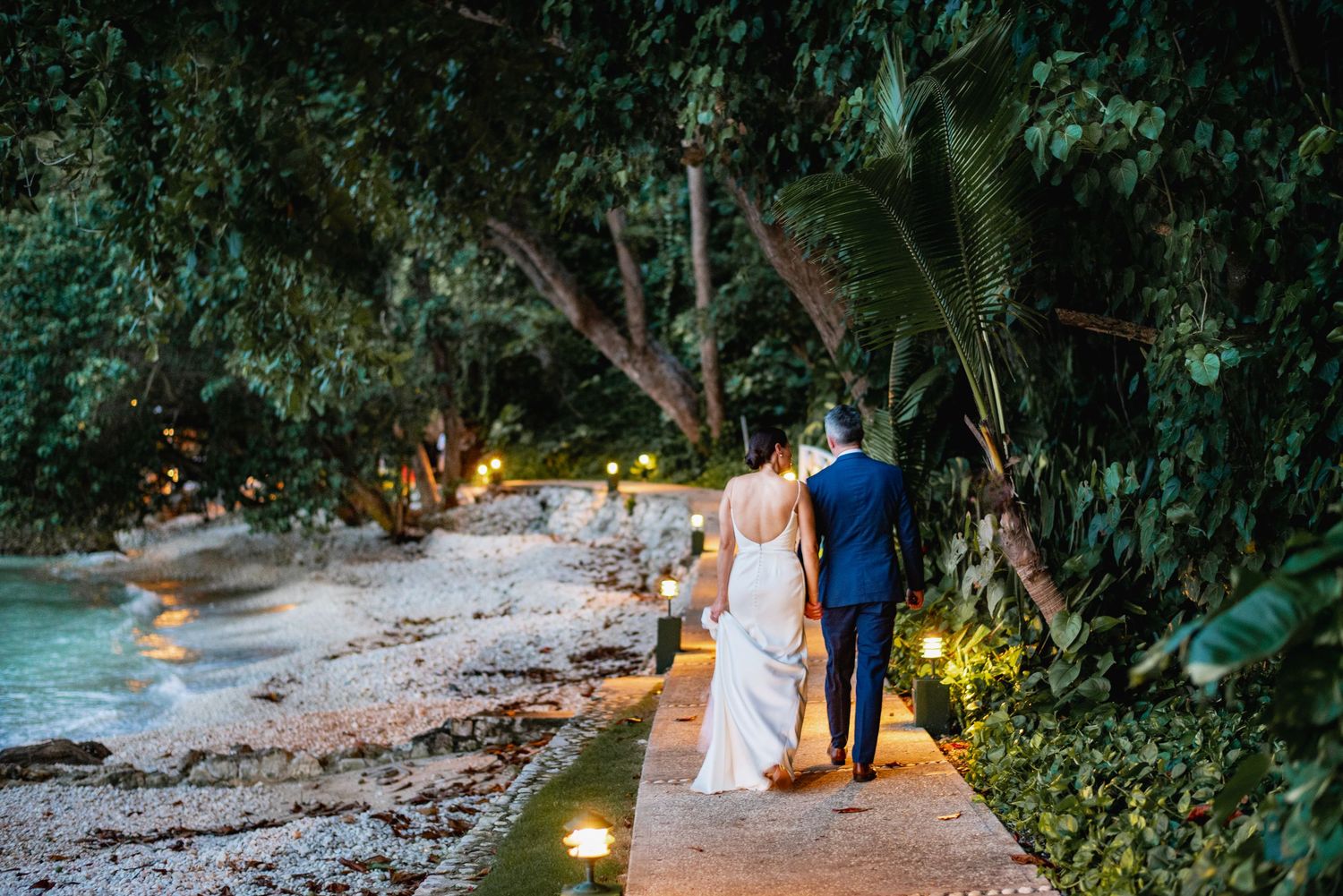 Romantic garden pathway illuminated by warm glowing lights at dusk with couple walking through lush greenery.