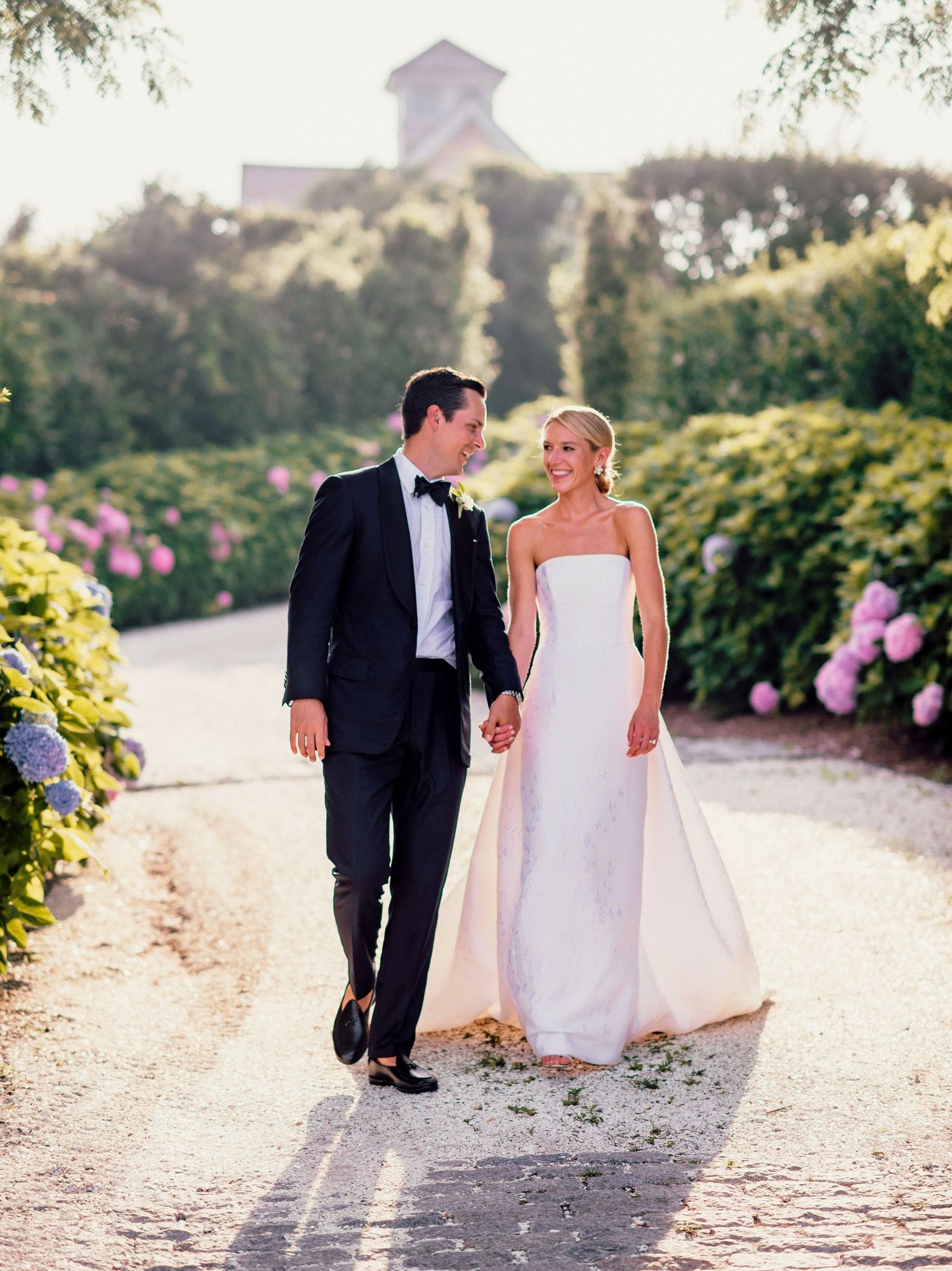 Bride and groom walking together on a romantic garden path during sunset.