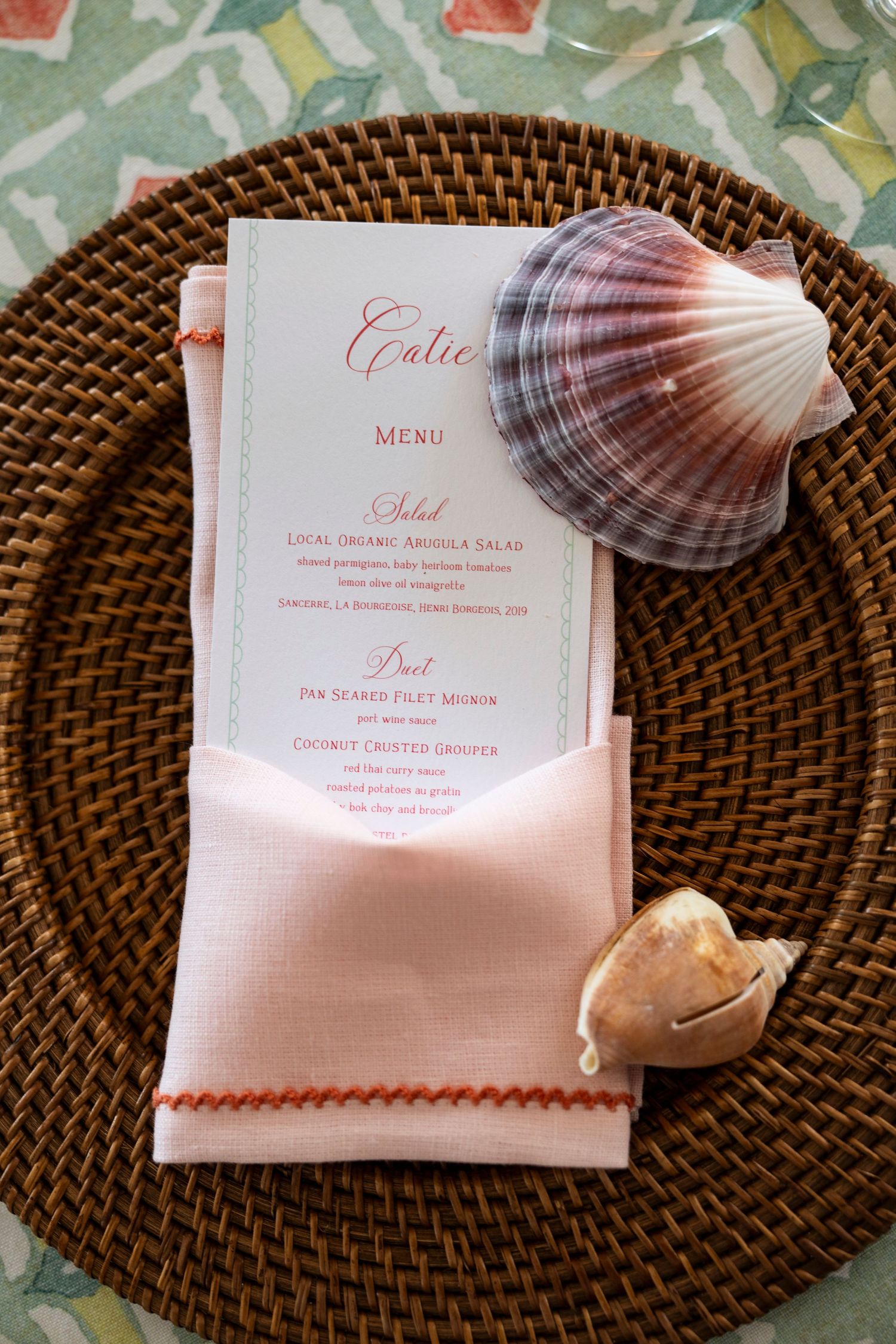 Wedding menu cards decorated with seashells on woven charger plates.
