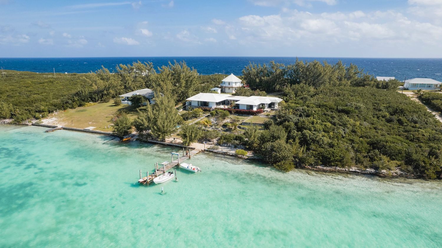 Aerial view of a coastal property with white buildings nestled among tropical vegetation beside crystal clear waters.