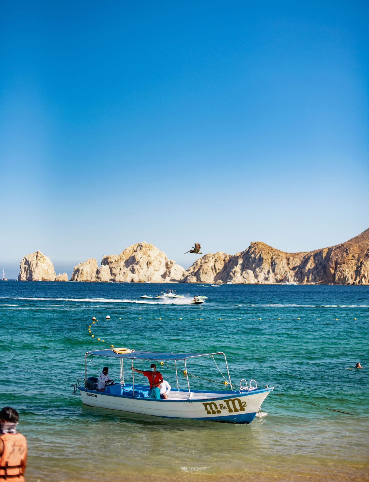 Turquoise waters of Cabo San Lucas beach with boats and iconic rock formations in background.