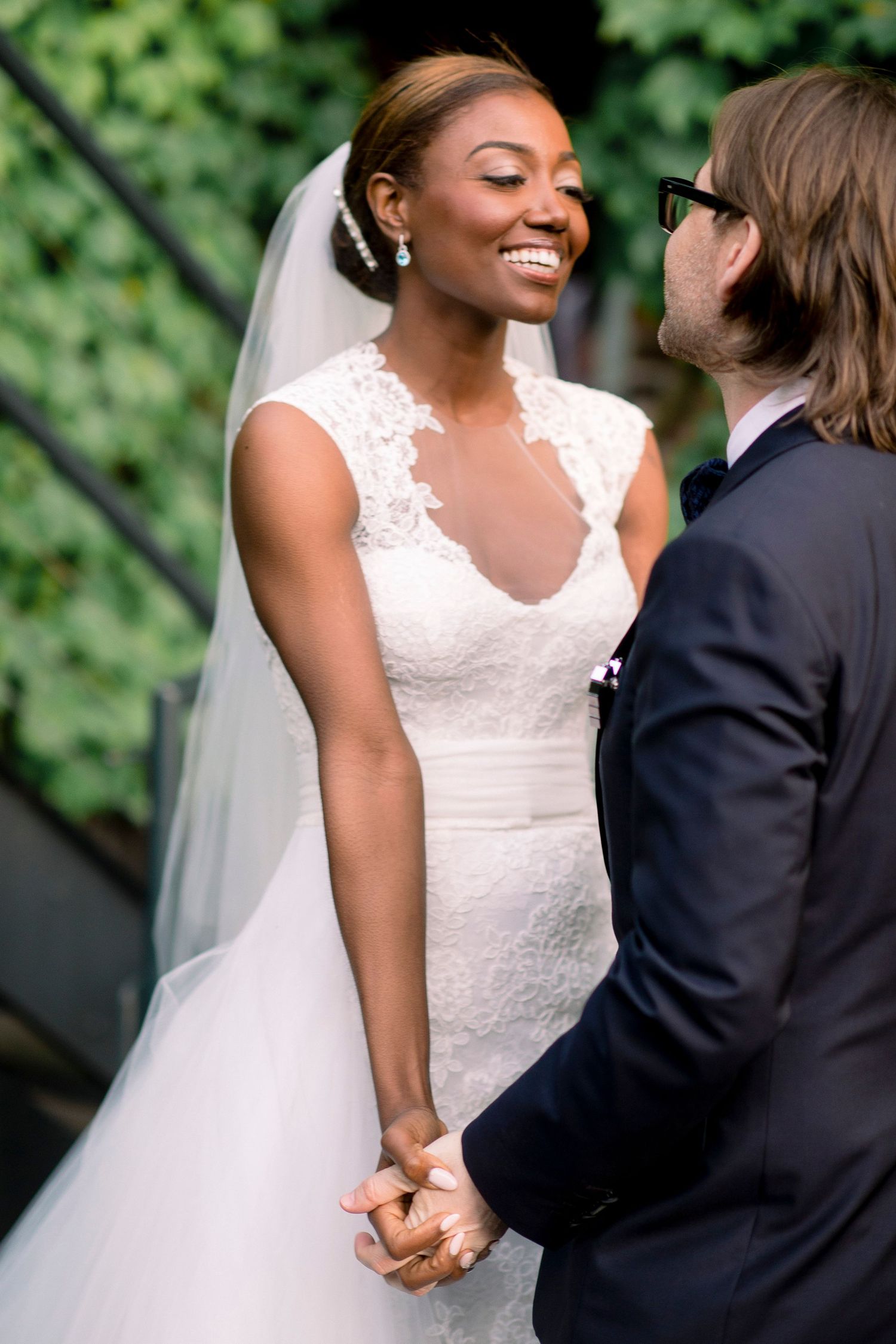 A happy couple shares an intimate moment during their wedding photoshoot against a lush green backdrop.