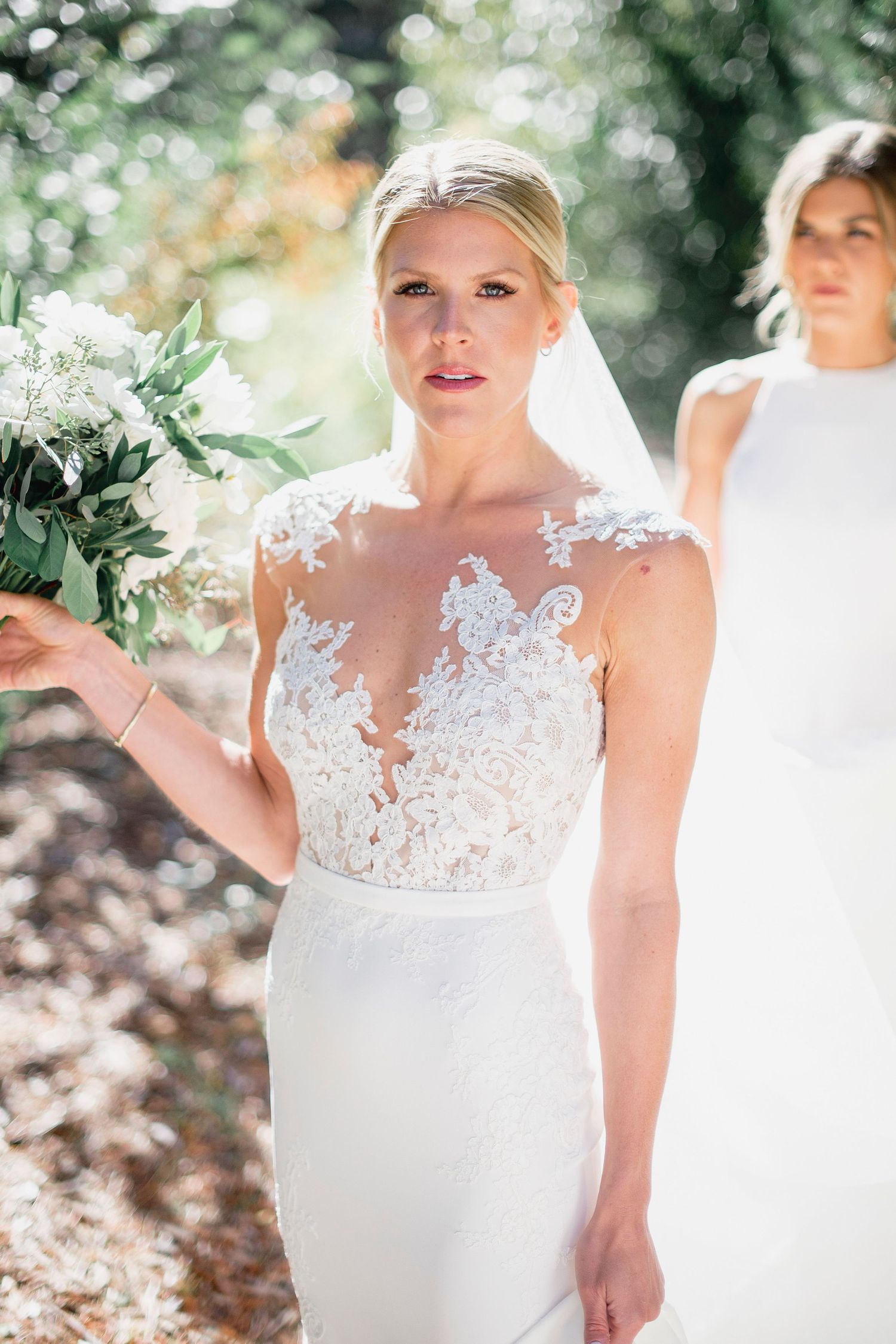 Bride wearing delicate lace wedding gown poses in natural outdoor setting.