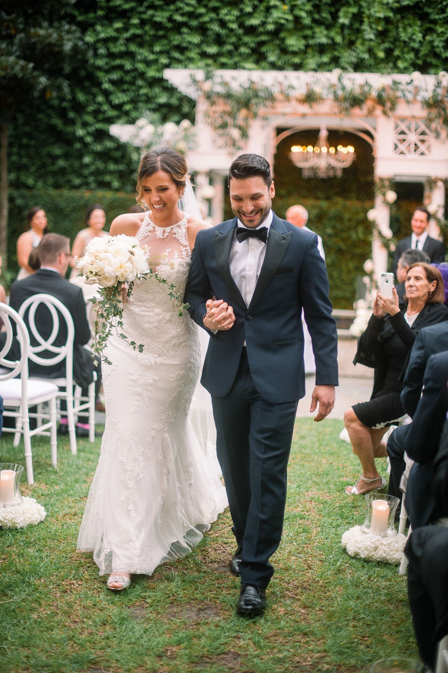 Couples dance together on a grassy lawn during an outdoor wedding reception with white chairs in the background.