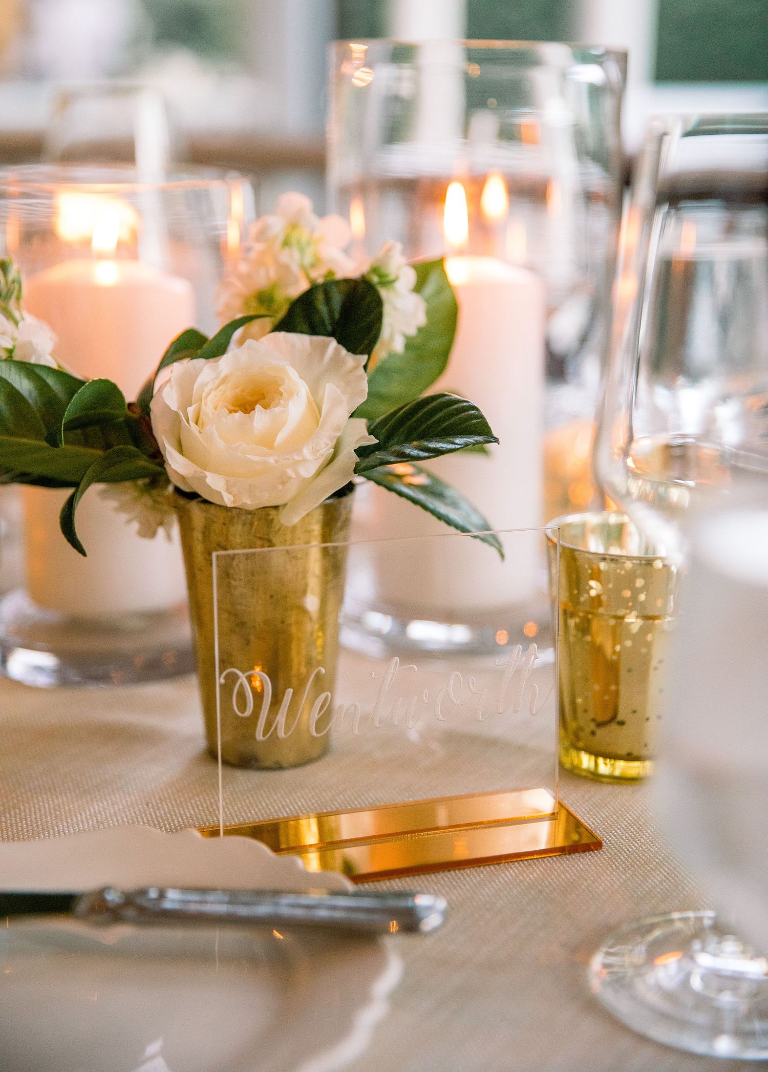 Elegant table setting with gold mercury glass vases holding white roses and glowing candles in a romantic atmosphere.