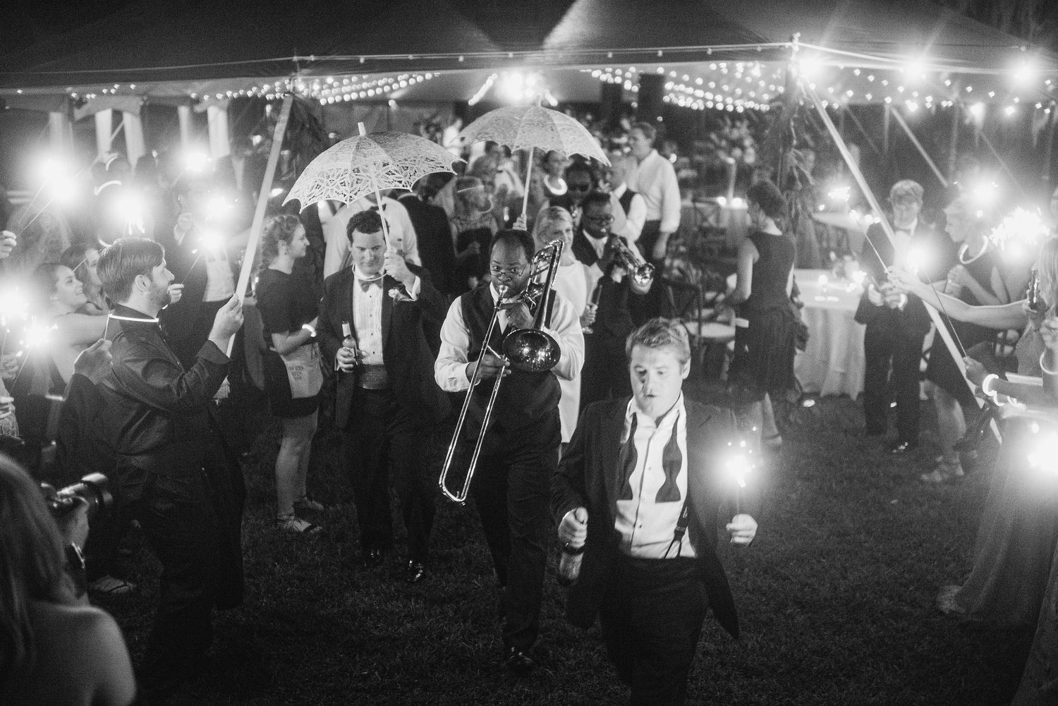 Wedding guests hold sparklers creating a magical light tunnel at an outdoor nighttime reception celebration.