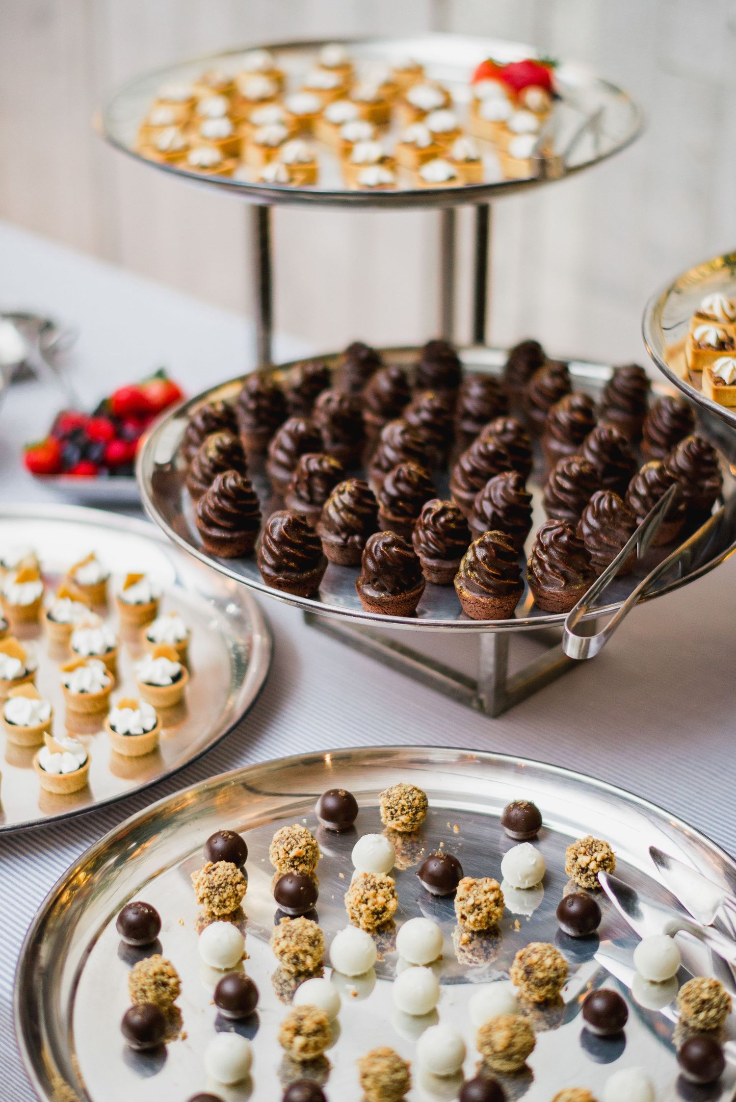 Elegant dessert display featuring chocolate truffles and assorted candies arranged on tiered silver platters at a catering event.