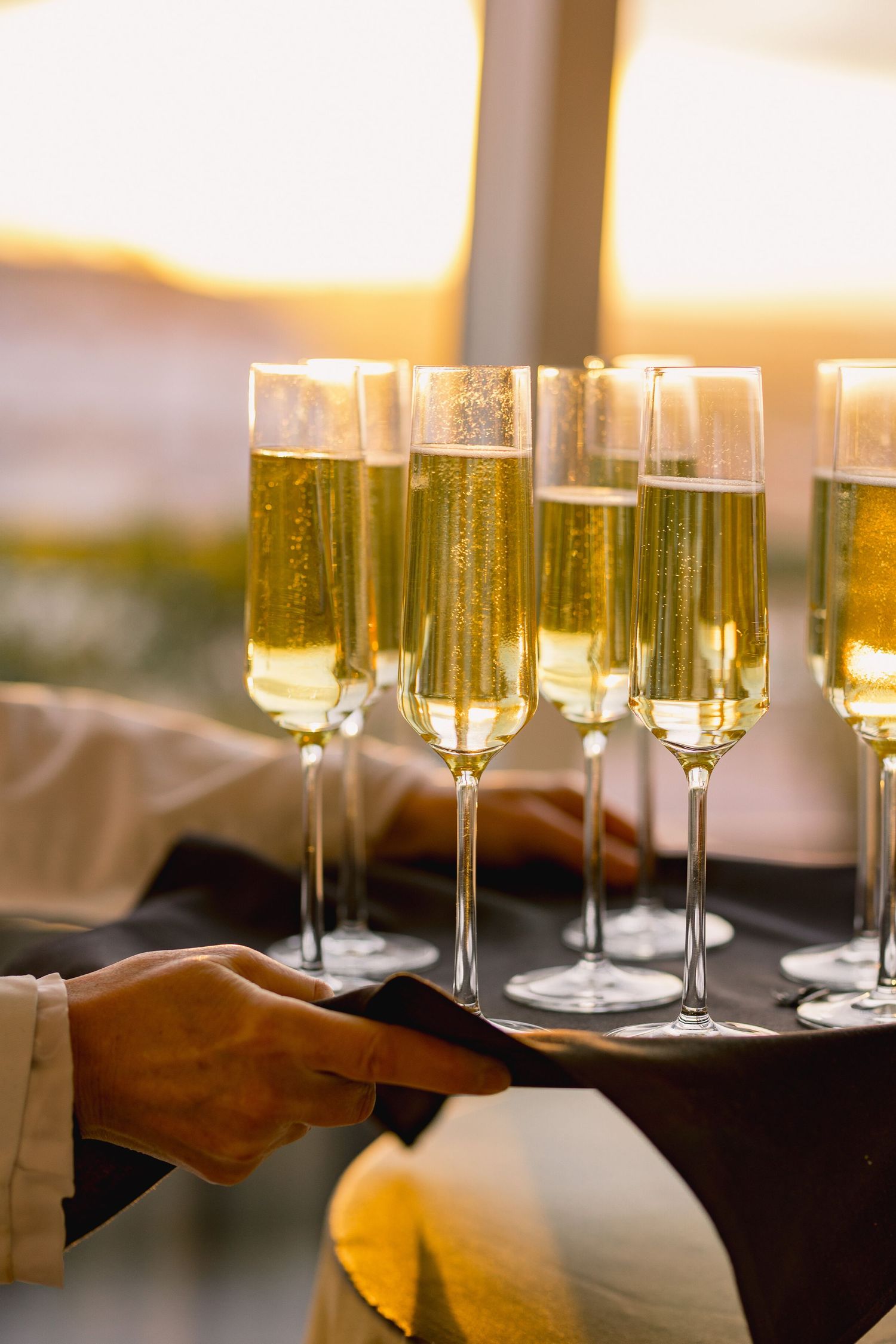 A server carries a tray of champagne flutes filled with sparkling wine at an elegant event.