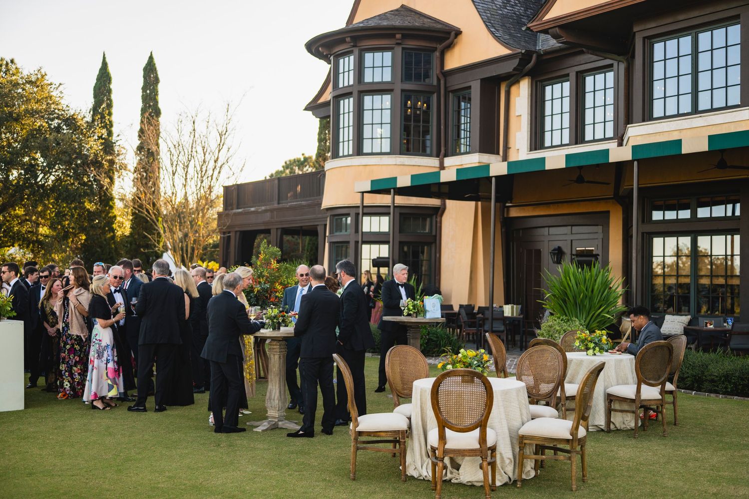 Elegant outdoor wedding reception setup with white chairs and tables arranged on a manicured lawn at sunset.