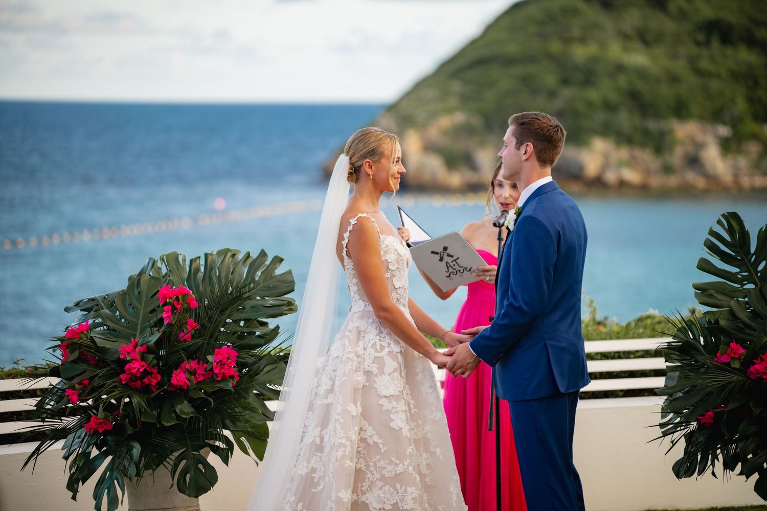 Tropical wedding ceremony with red flowers and palm leaves decorating oceanfront terrace.