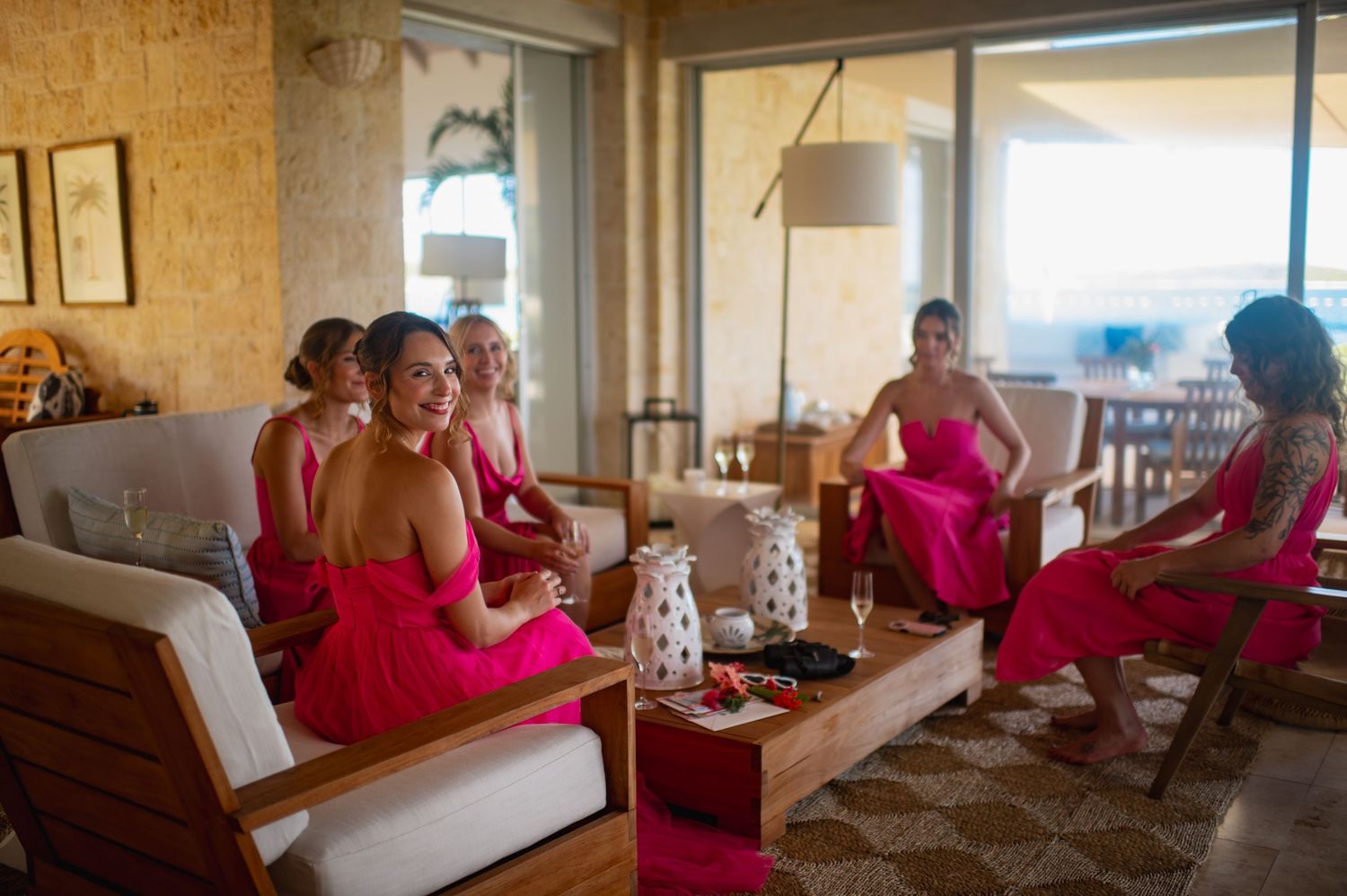 A group in red dresses sits on a white couch in a sunlit room during a social gathering.