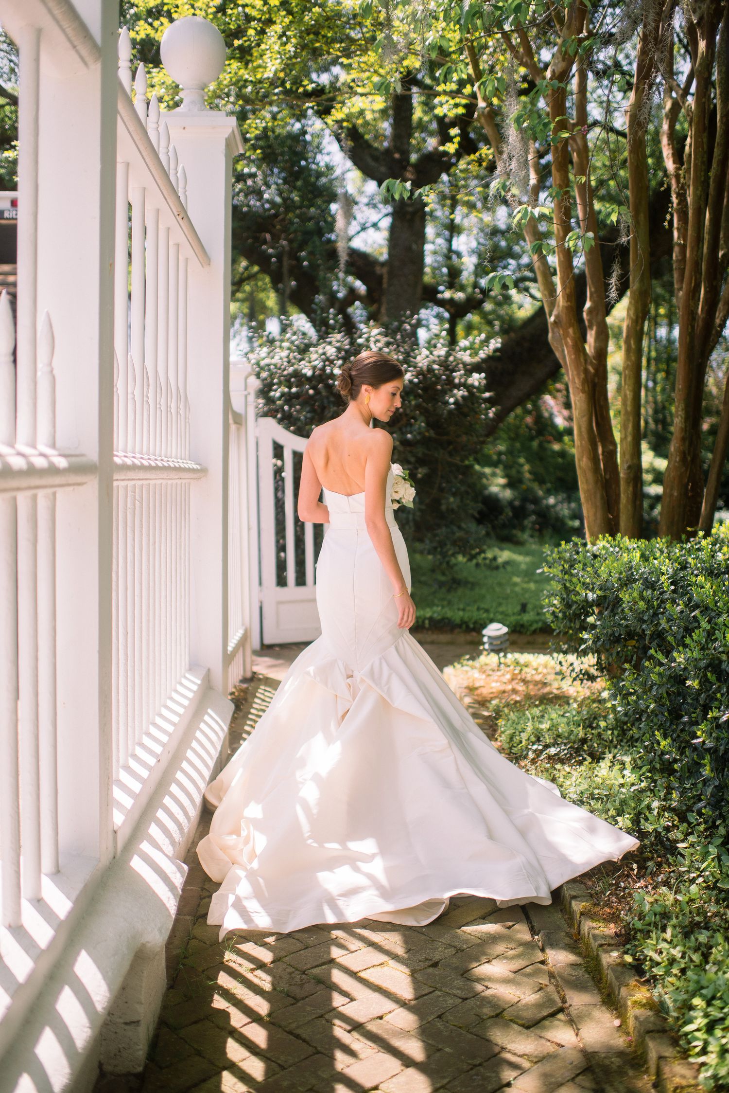 A bride in a flowing white ball gown twirls gracefully on a sunlit porch with white columns and lush greenery.