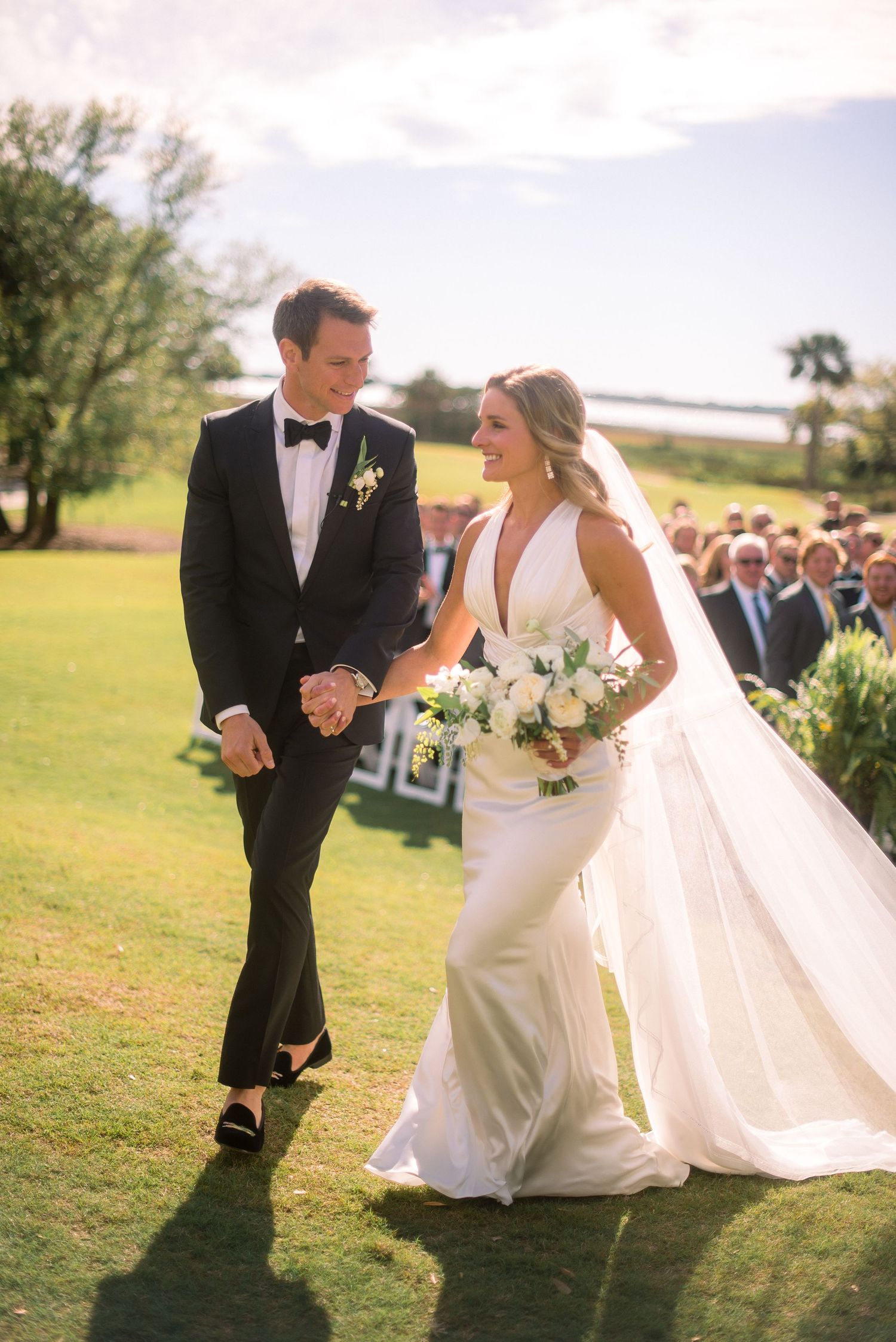 Newlyweds share joyful moments together on a grassy field during their wedding photo session.
