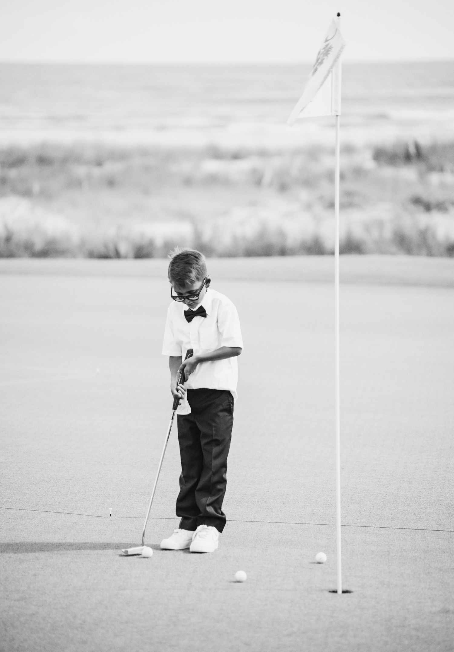 Young golfer in formal attire practicing putting on a golf course.