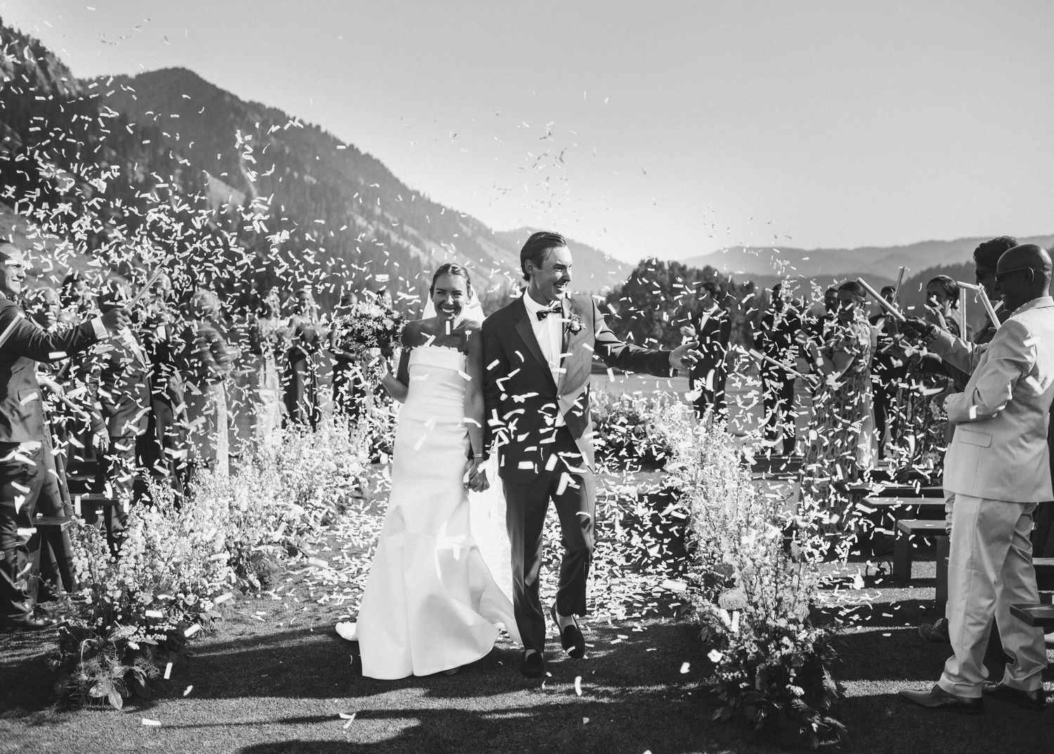 A black and white panoramic view of people walking through an orchard with blossoming trees in springtime.