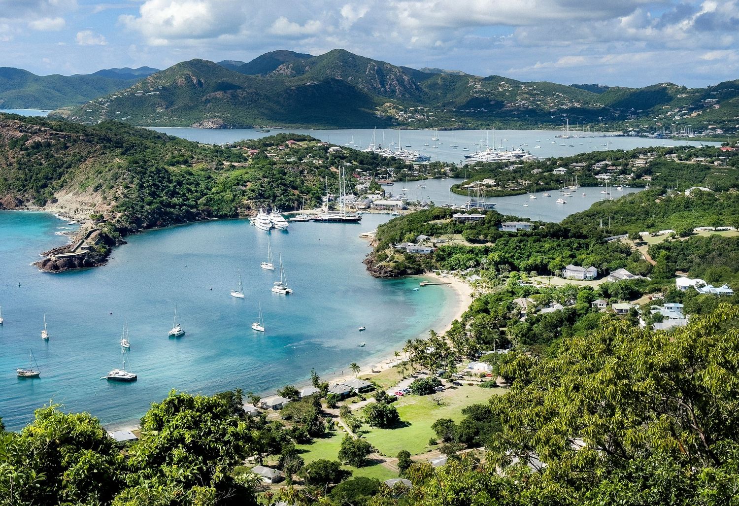Panoramic view of a tropical bay with boats anchored and lush green mountains in the background.