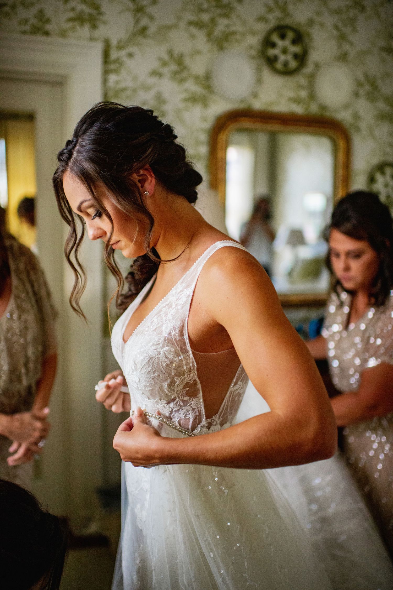 A bride in a white lace wedding dress adjusts her gown while getting ready for her special day.