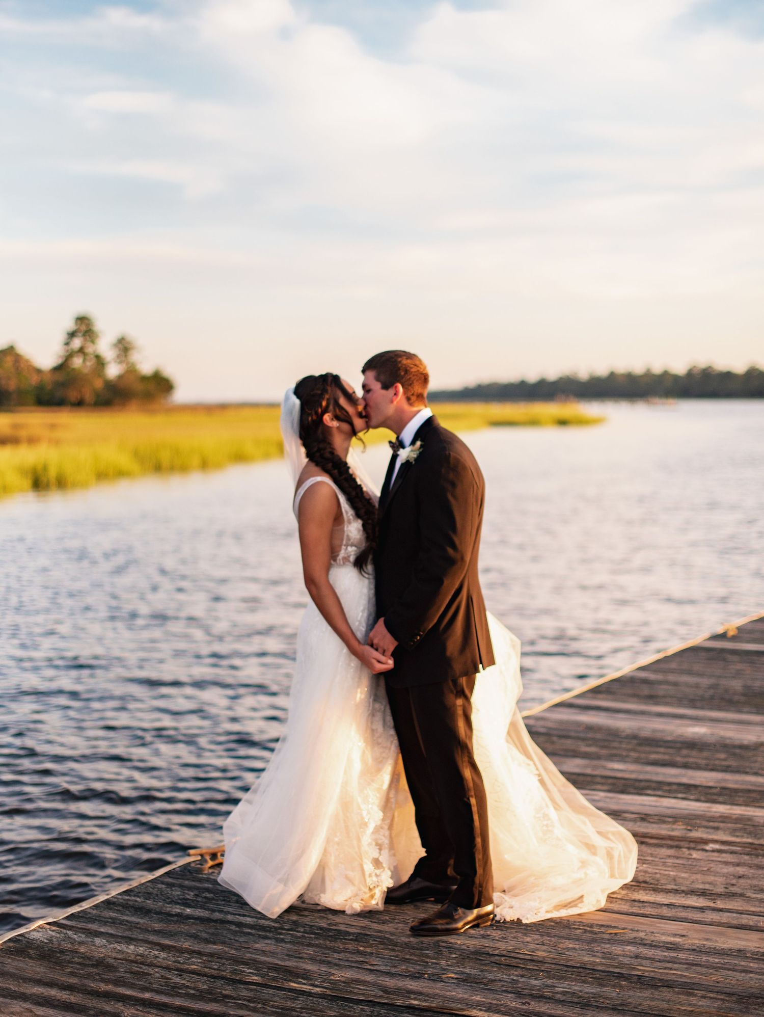 A couple shares a romantic moment on a wooden dock at sunset by a serene lake.