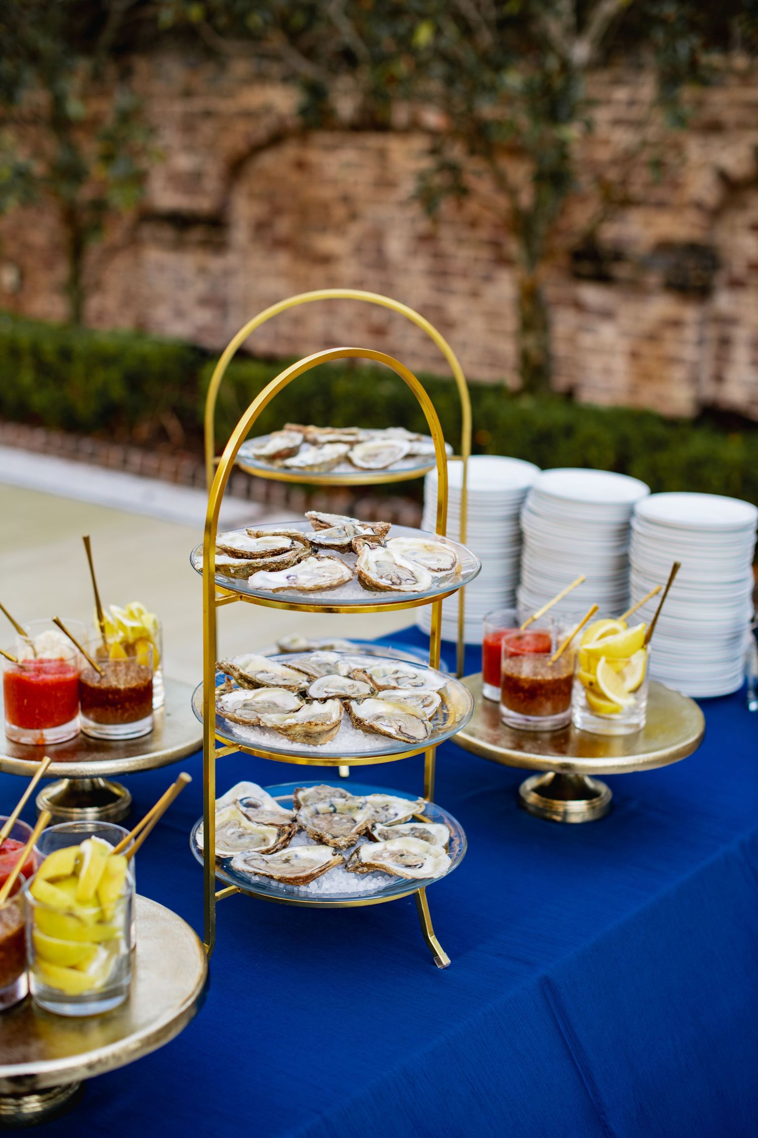 Multi-tiered serving platters with sandwiches and snacks arranged on a blue tablecloth at a catered event.