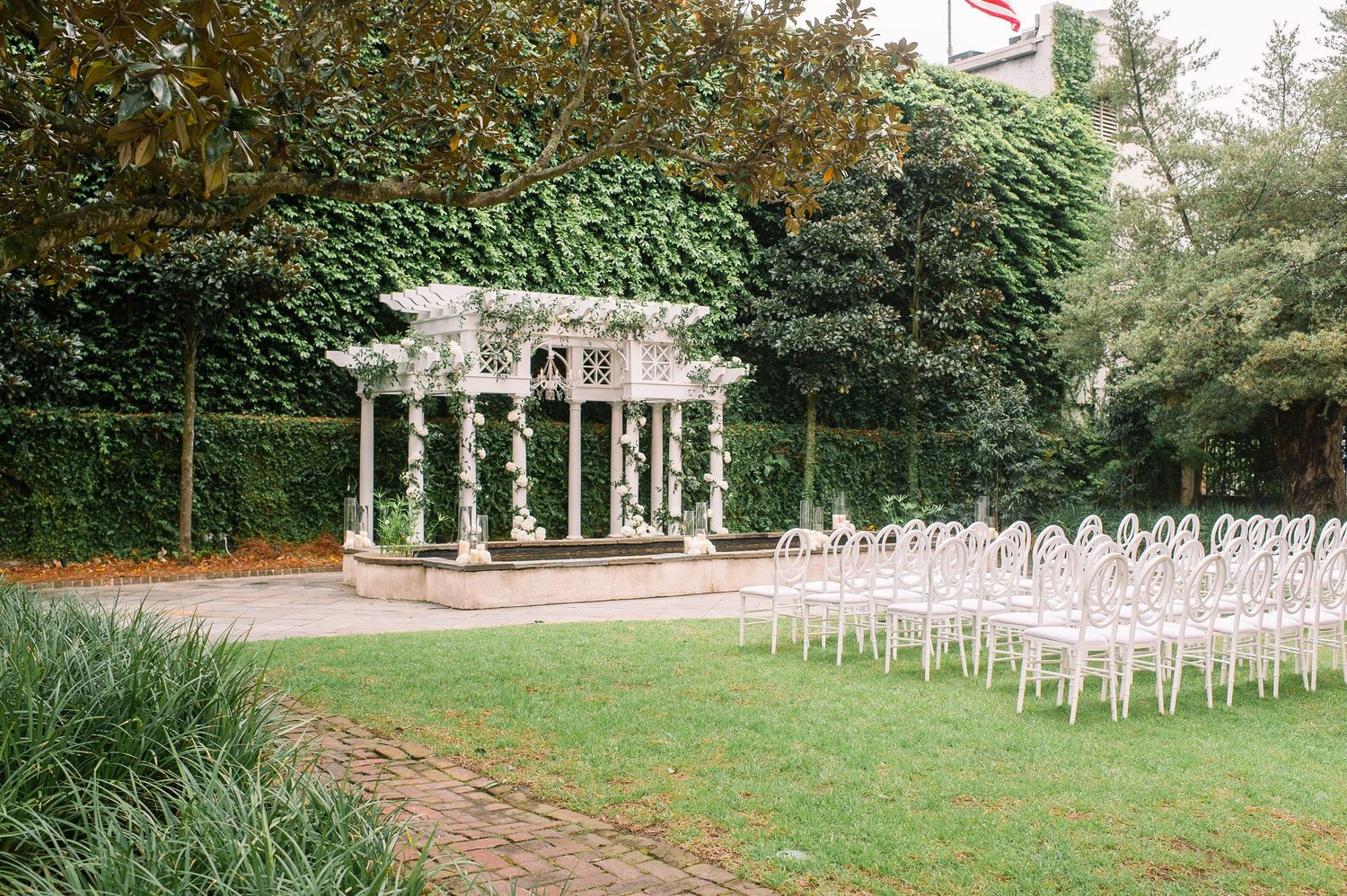 White garden gazebo set up for an outdoor wedding ceremony with rows of white chairs on a manicured lawn.