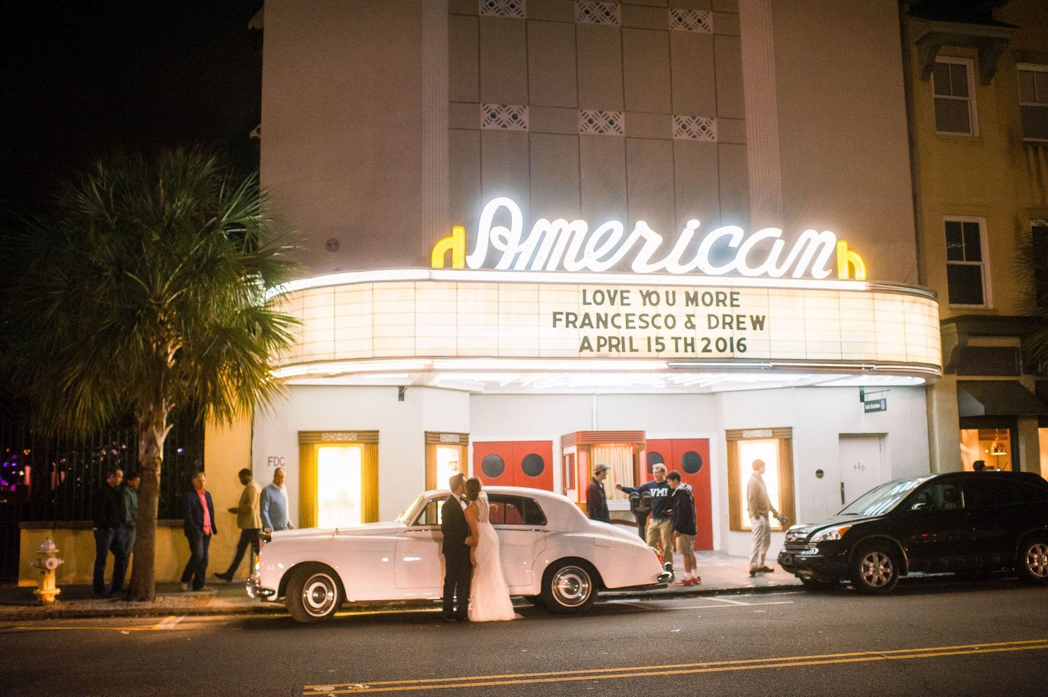 Illuminated vintage American Theater facade at night with neon signage and palm trees in Charleston, South Carolina.