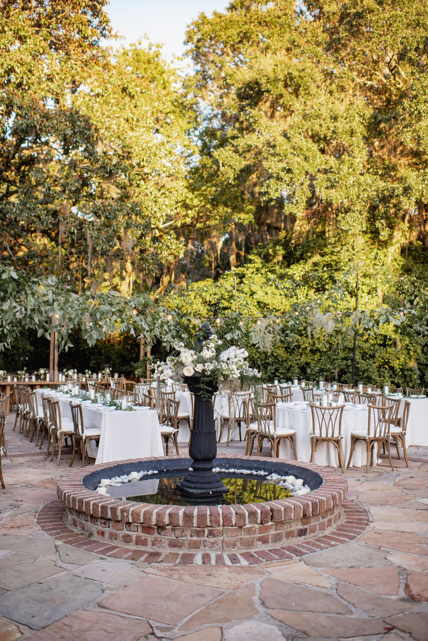 Outdoor wedding reception venue with circular brick patio and wooden chairs arranged under autumn trees at sunset.