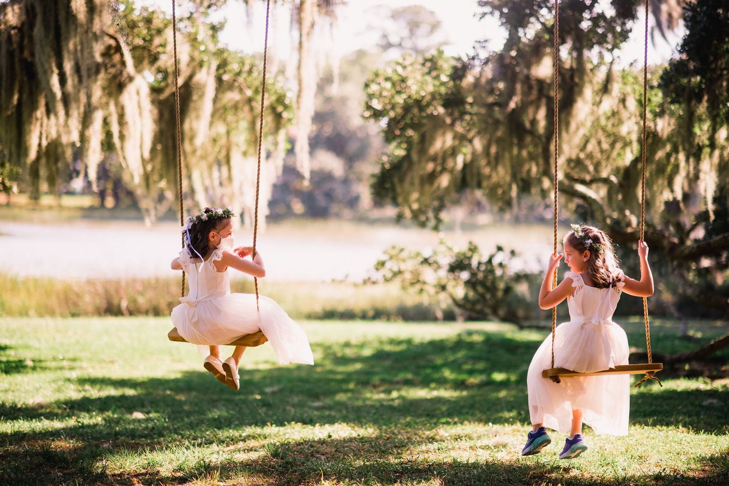 A wooden swing hangs from a large oak tree with Spanish moss during golden hour in a peaceful outdoor setting.
