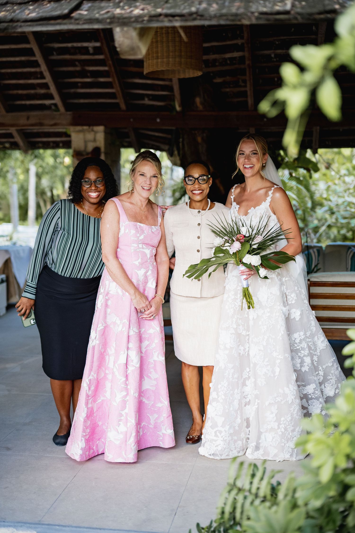 A group photo of wedding party members in formal attire standing under a covered outdoor area.