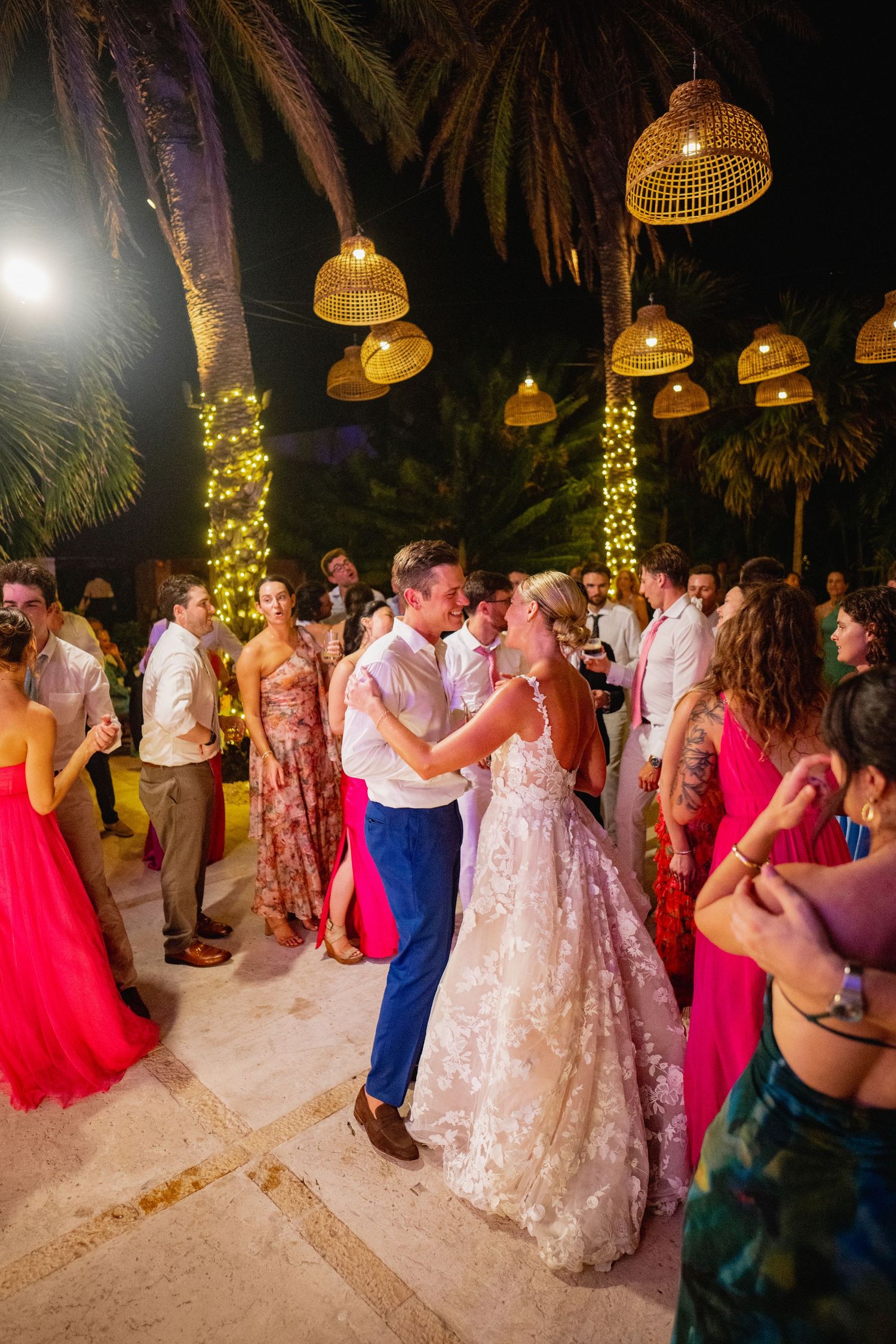 Evening beach wedding reception with hanging lanterns and string lights creating a magical atmosphere.