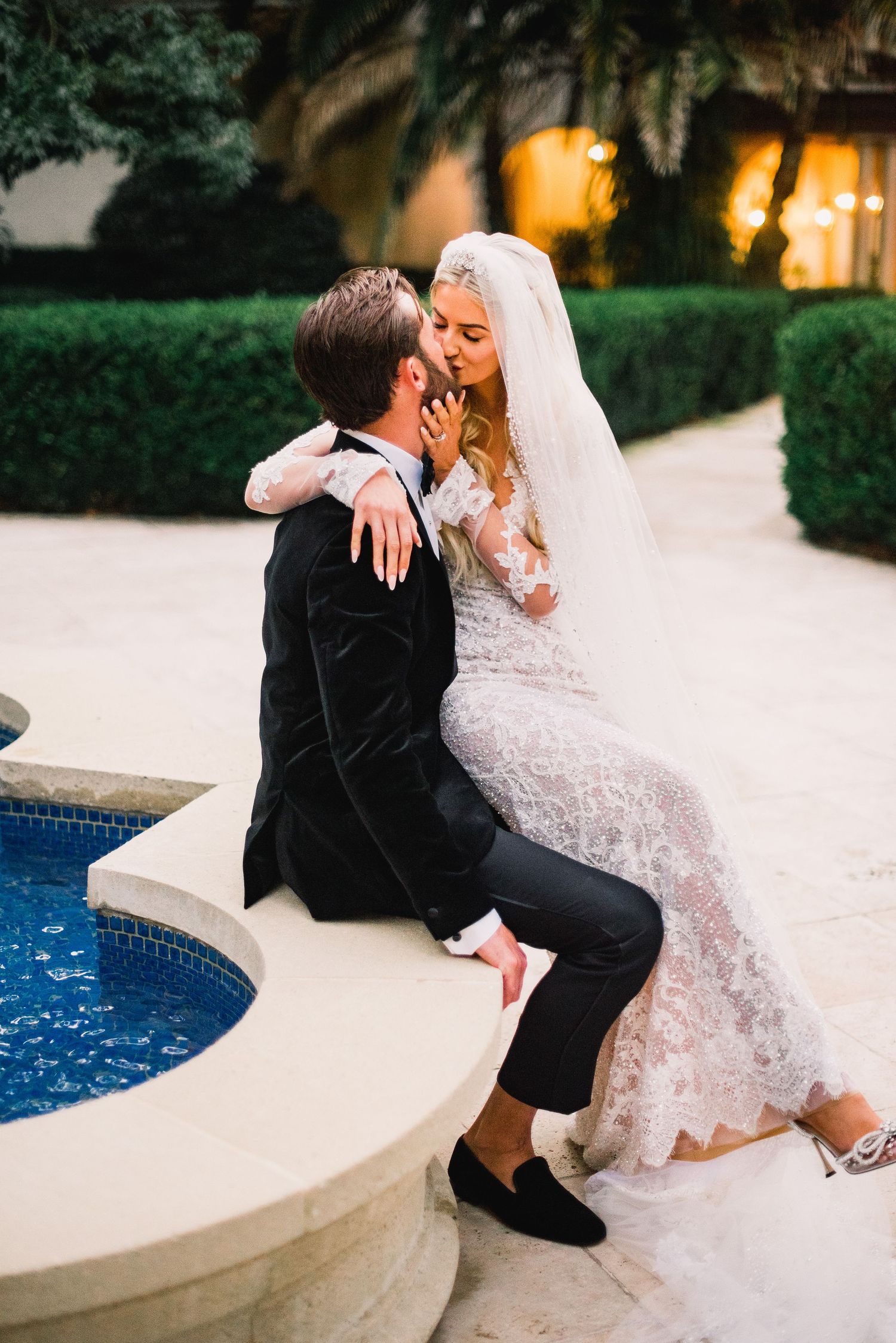 Romantic wedding couple shares intimate moments by a pool's edge in elegant formal attire.