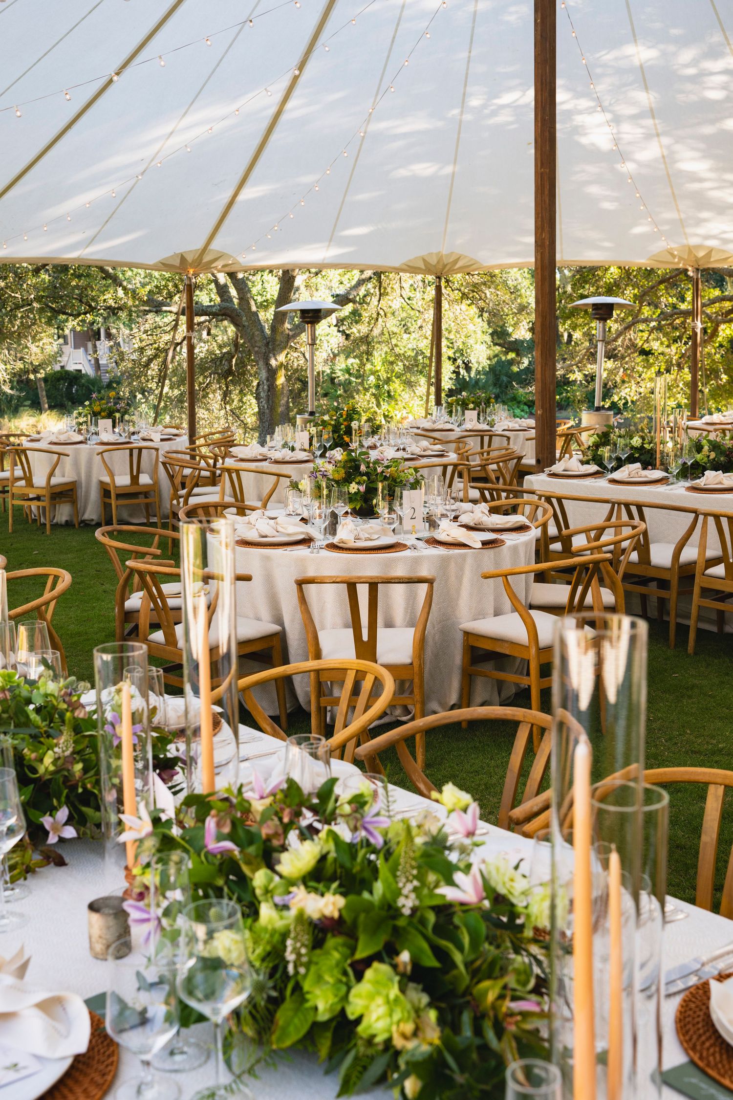 Elegant wedding reception tent setup with round tables, wooden chairs, and lush floral centerpieces under white canopy.